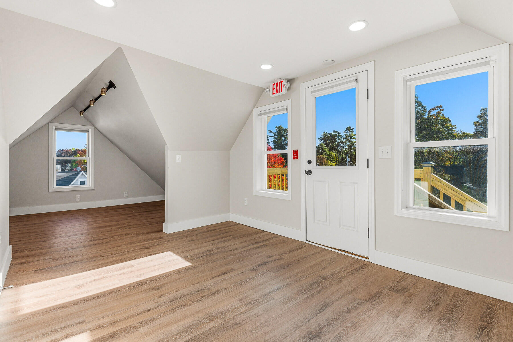 Vacant room with sloped ceilings, wood-look floors, and a door opening onto a wooden deck.