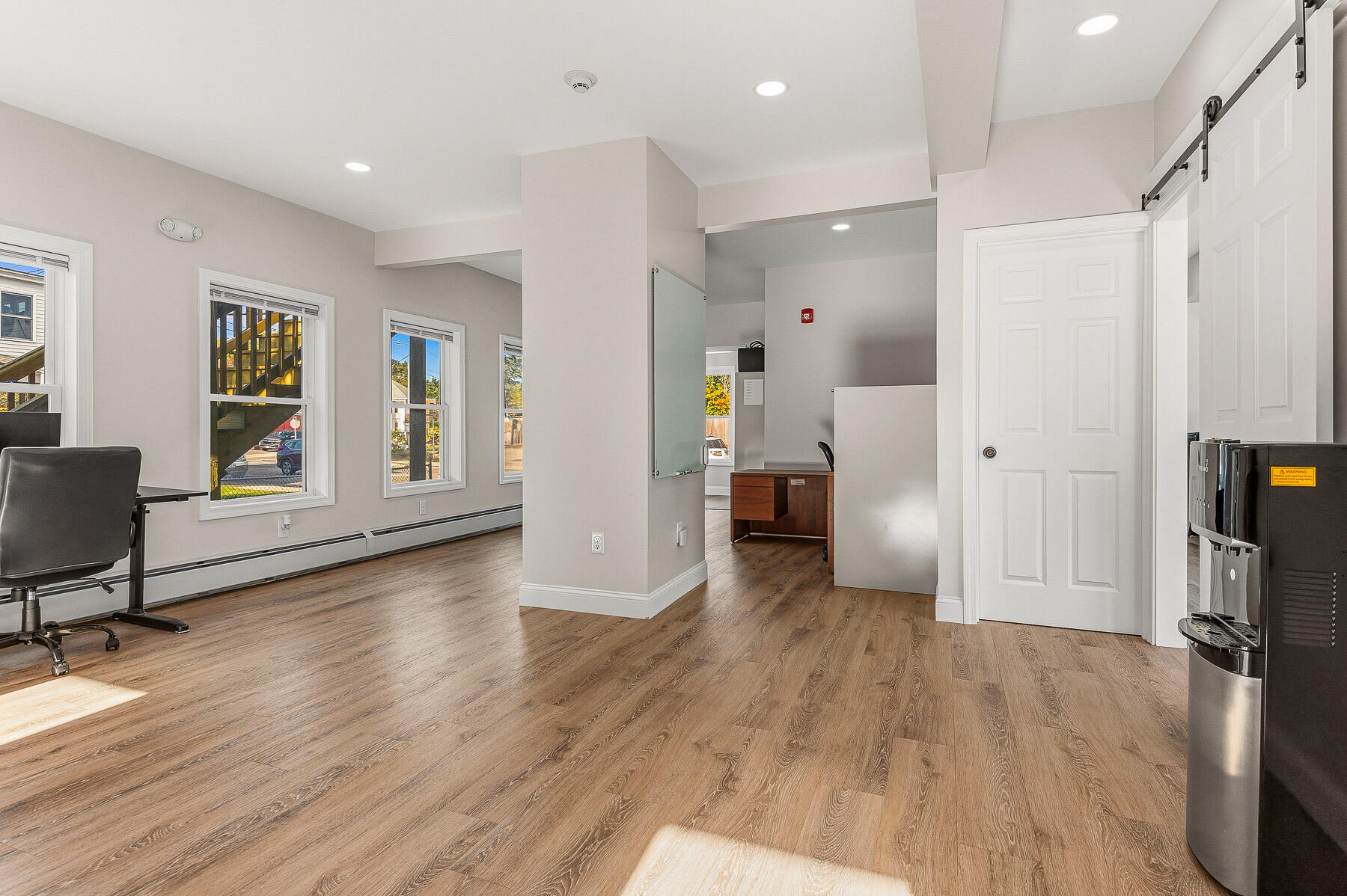Office interior with wood-look flooring, multiple windows, and a white sliding barn door.