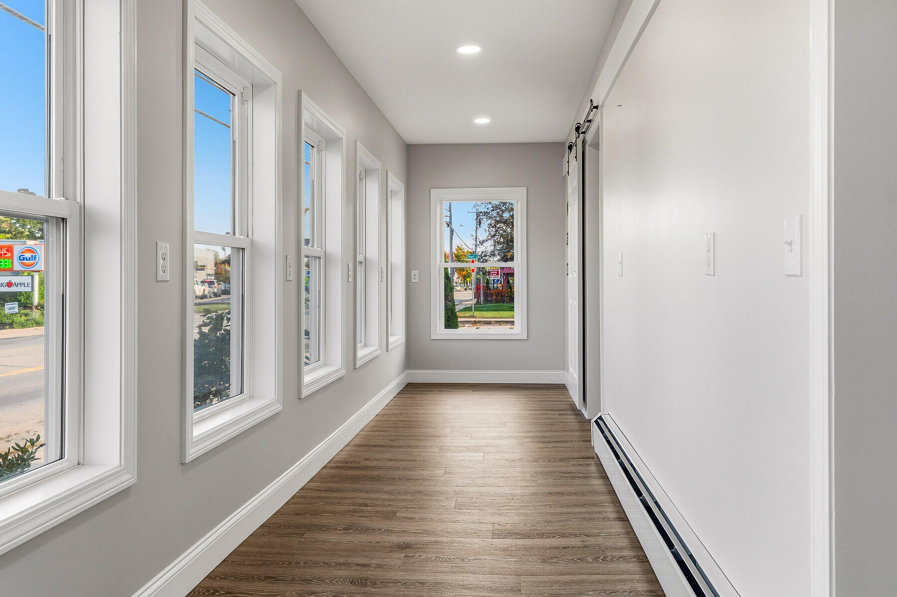 Vacant hallway with tall windows, wood-look floors, and a long baseboard heater.