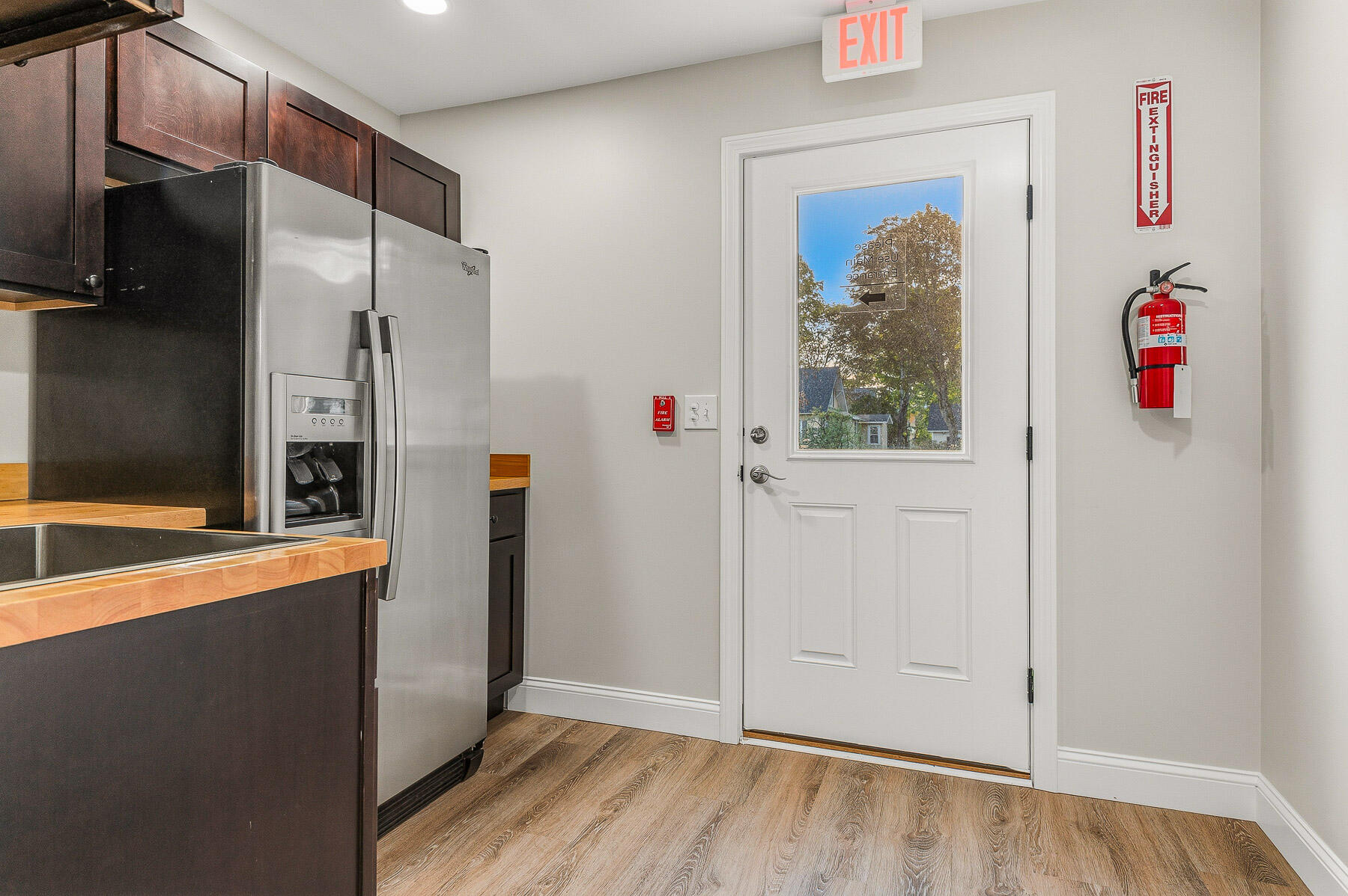 Kitchen with dark cabinets, butcher-block counters, stainless refrigerator, and a windowed exit door.