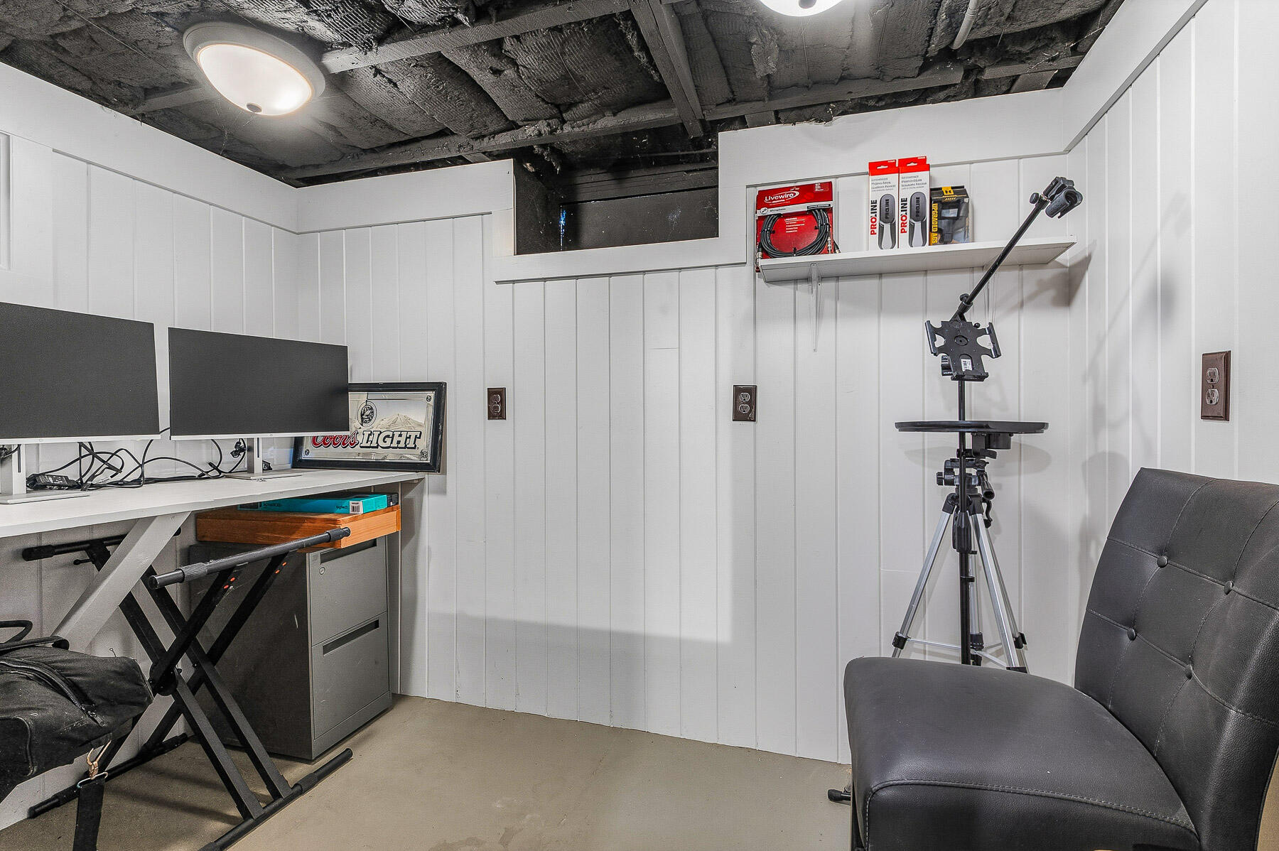 Workspace with dual monitors, a tripod-mounted device, and a black lounge chair beneath an exposed ceiling.