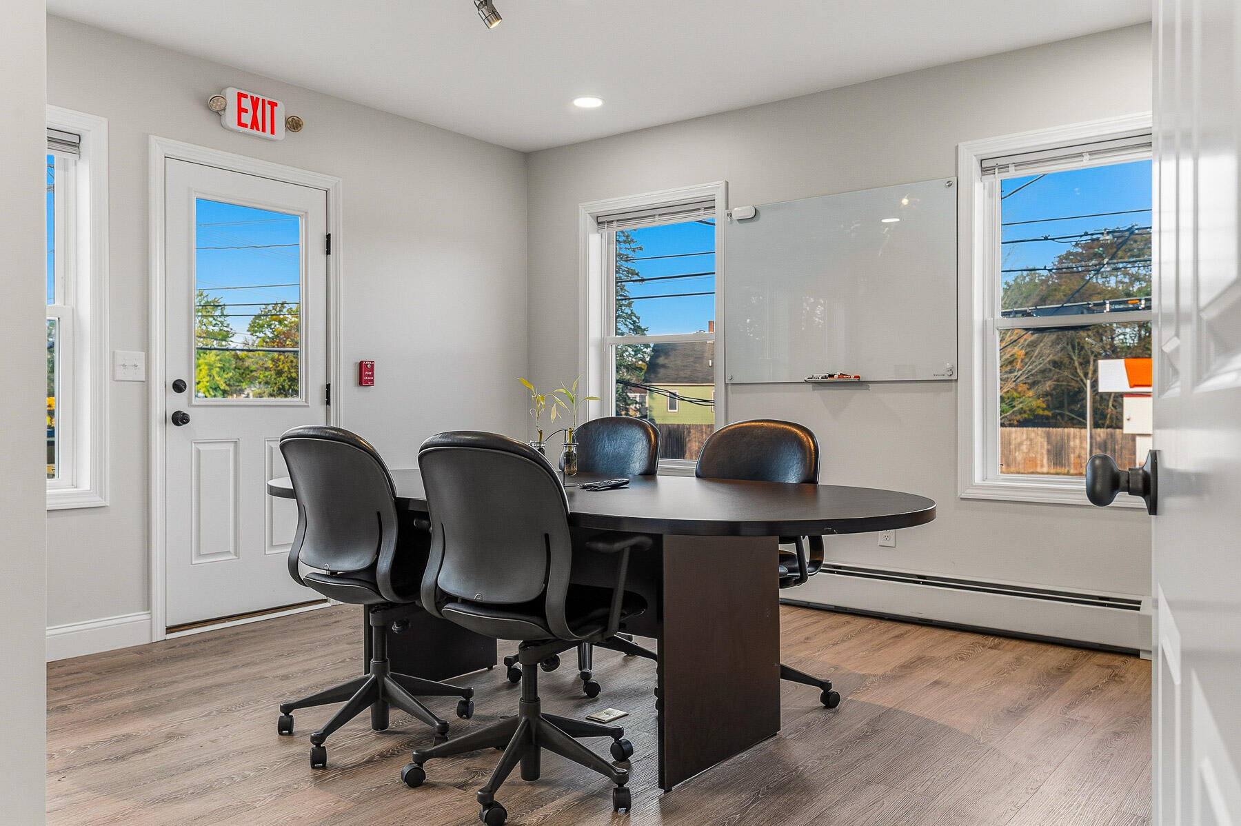 Office conference room with an oval meeting table, black chairs, and a wall-mounted whiteboard.