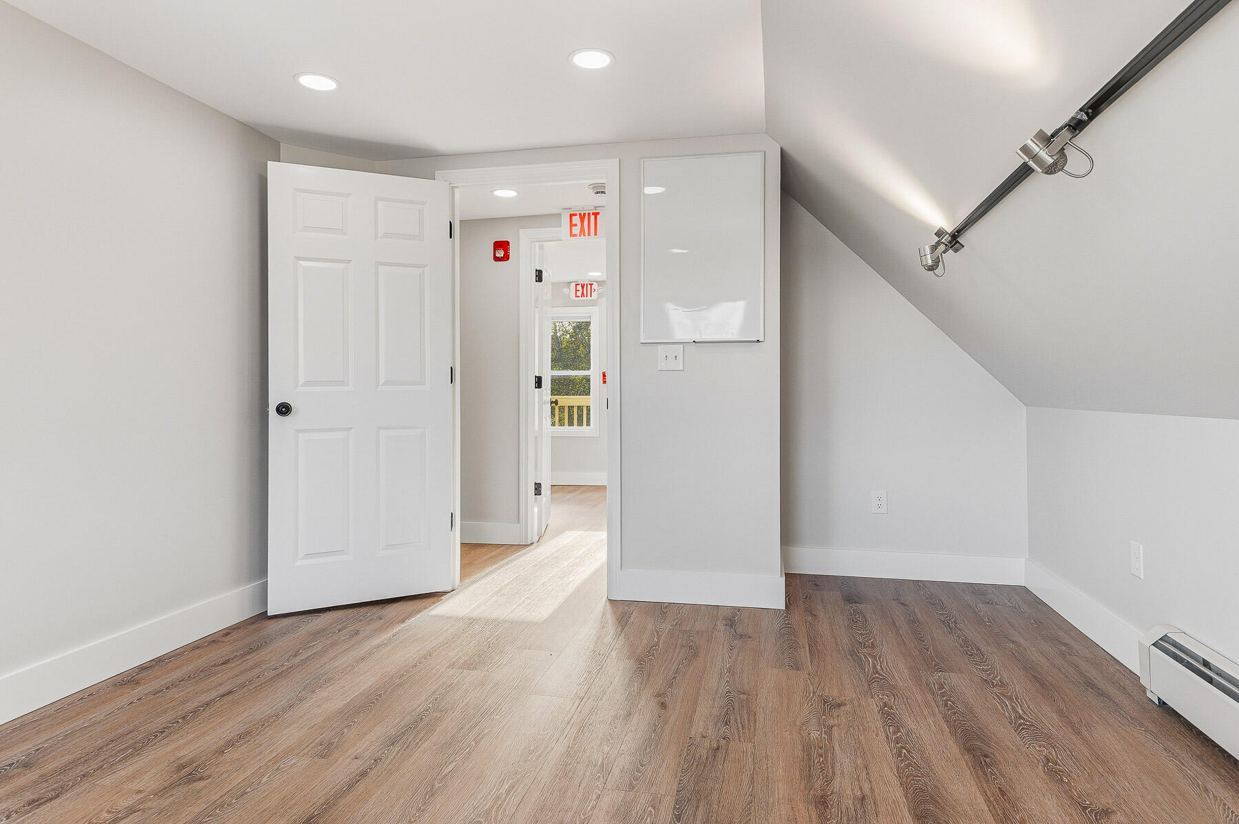 Vacant room with wood-look flooring, a sloped ceiling, and an open doorway to an EXIT-marked hall.
