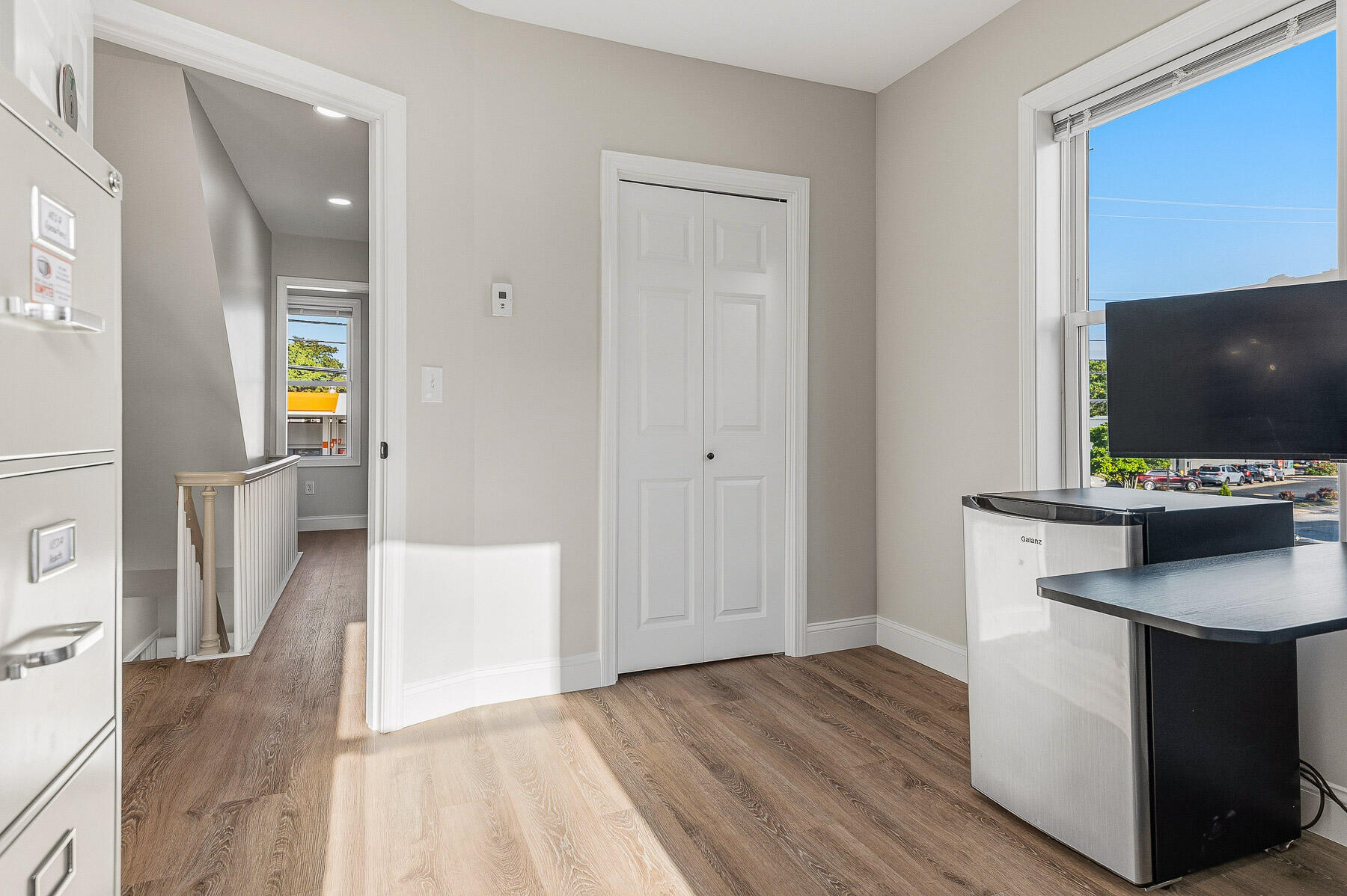 Bright room with wood-look flooring, a large window, and refrigerators beside a dark countertop.