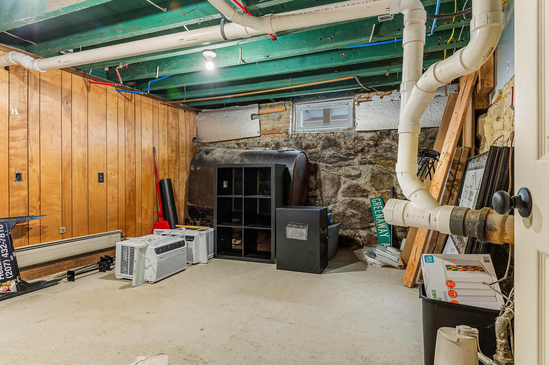 Unfinished basement with exposed pipes and joists, a stone foundation, and heating equipment.