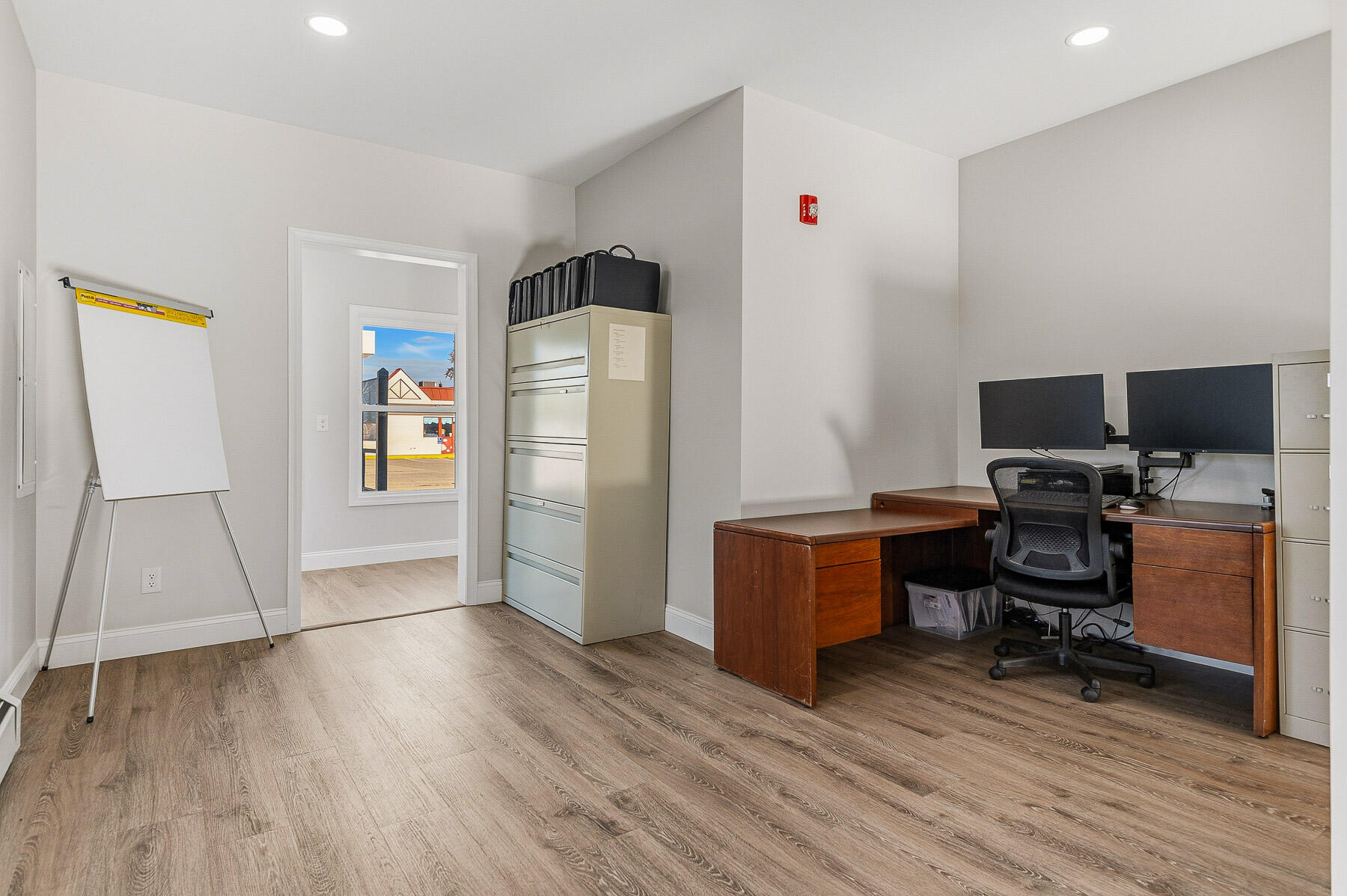 Office with wooden desks, computer monitors, metal filing cabinets, and a flip chart.