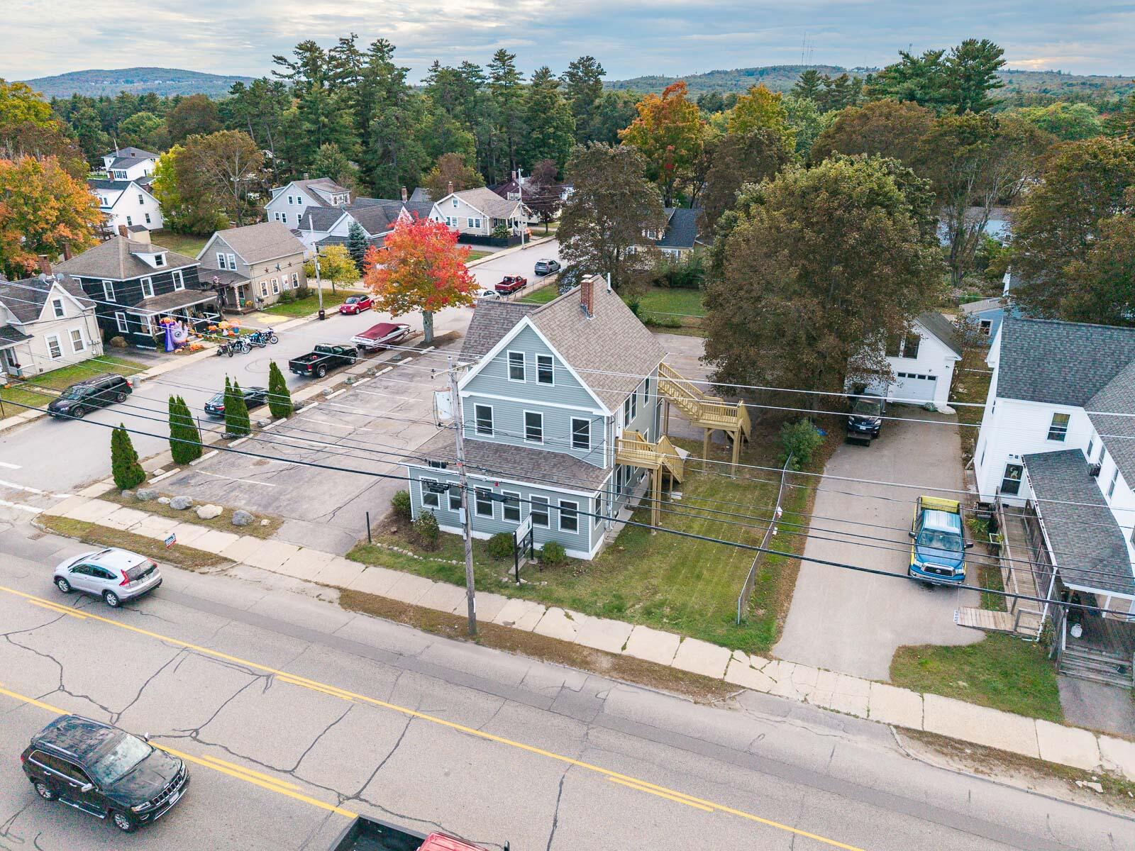 Gray multi-story building beside a road, surrounded by homes and autumn trees.