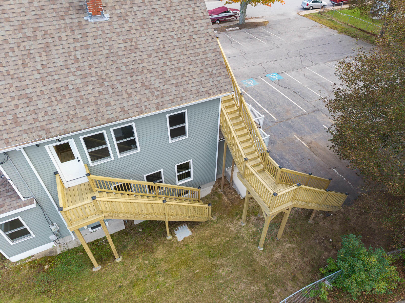 Aerial view of a gray-sided building with elevated wooden decks and staircases beside a parking lot.