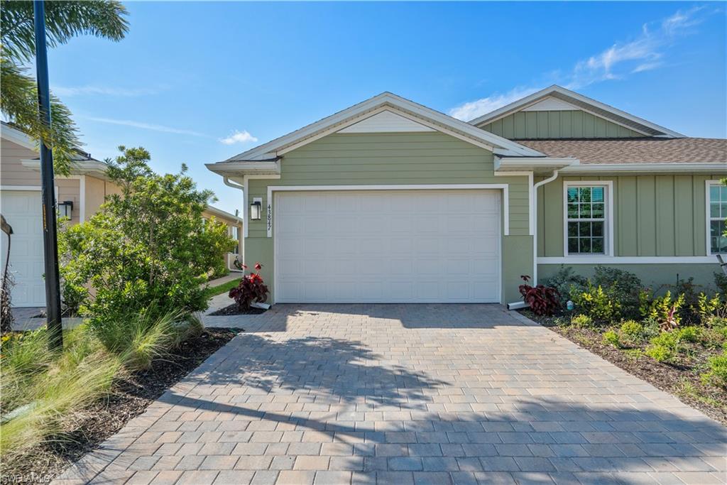 Green single-story home with a white double garage and paved driveway.