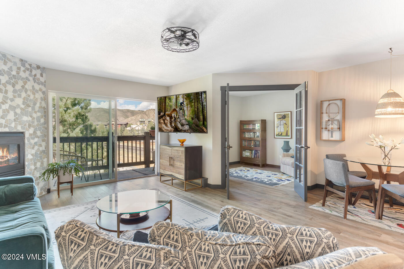 Living room with a stone fireplace and balcony doors overlooking mountain views.