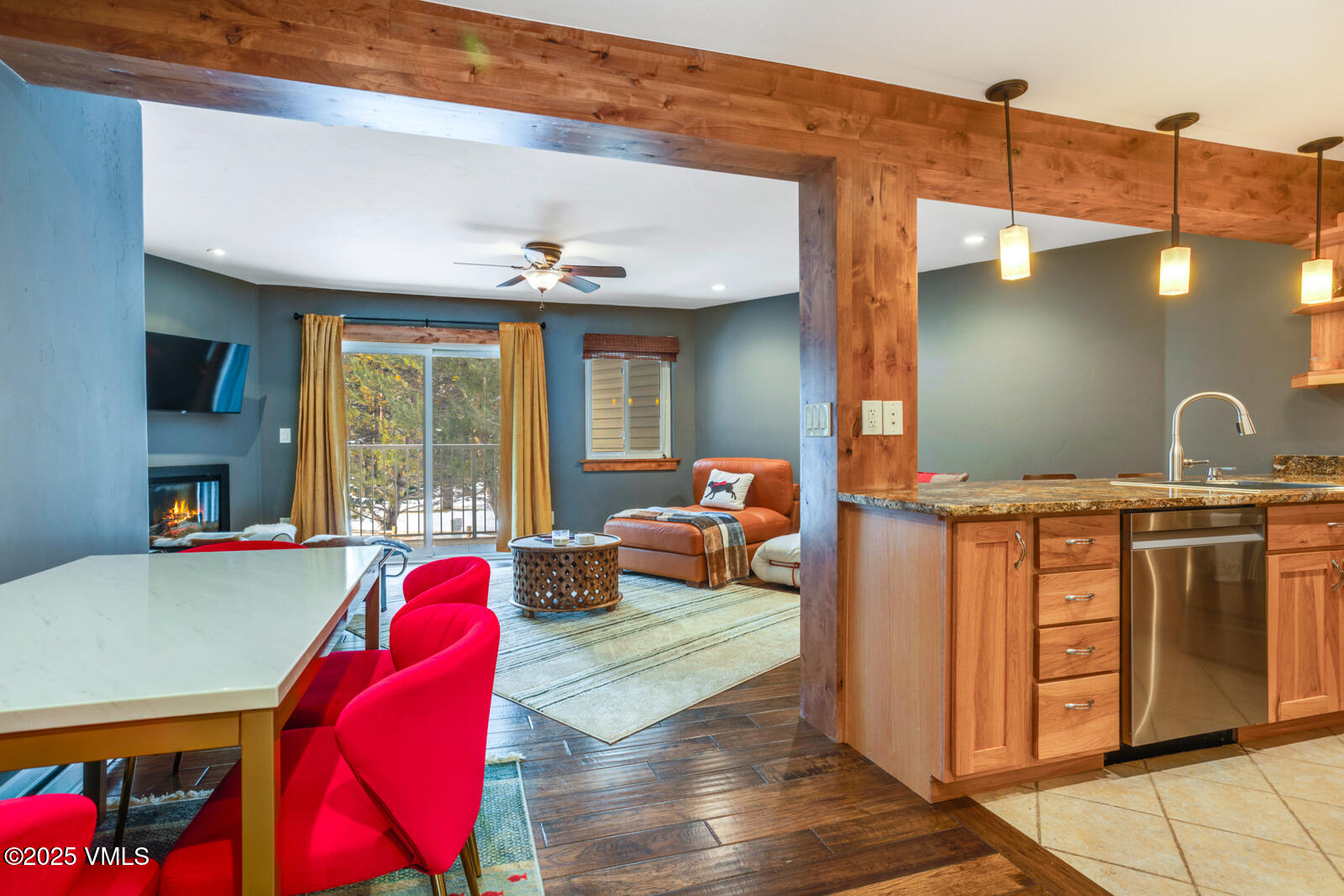 Open-plan living room and kitchen with wood beams, red chairs, and a fireplace.