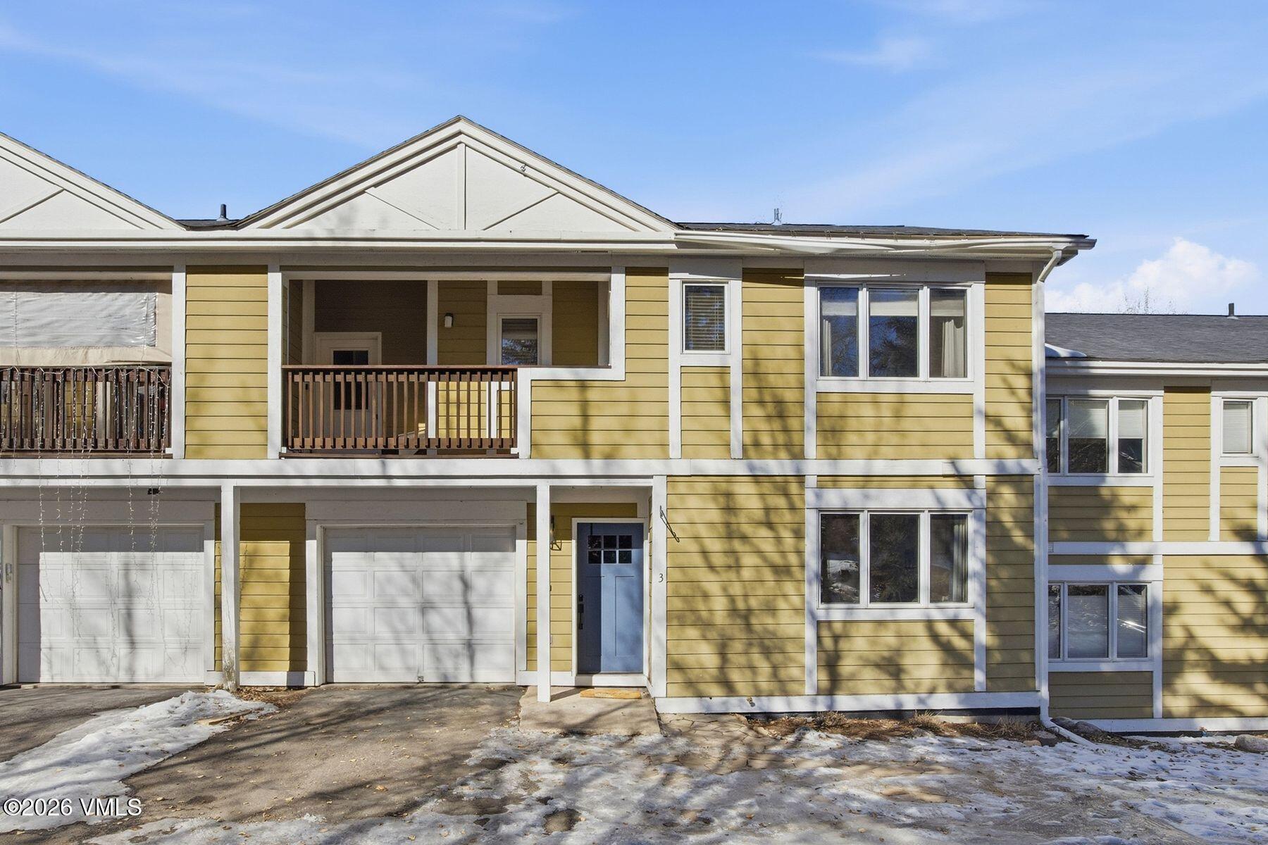 Yellow-sided residential building with upper balconies, garage doors, and a blue entrance door.