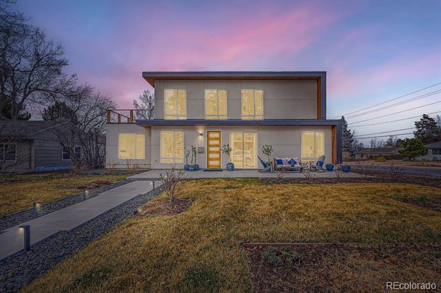 Modern two-story home with illuminated windows and a walkway across the front lawn at dusk.