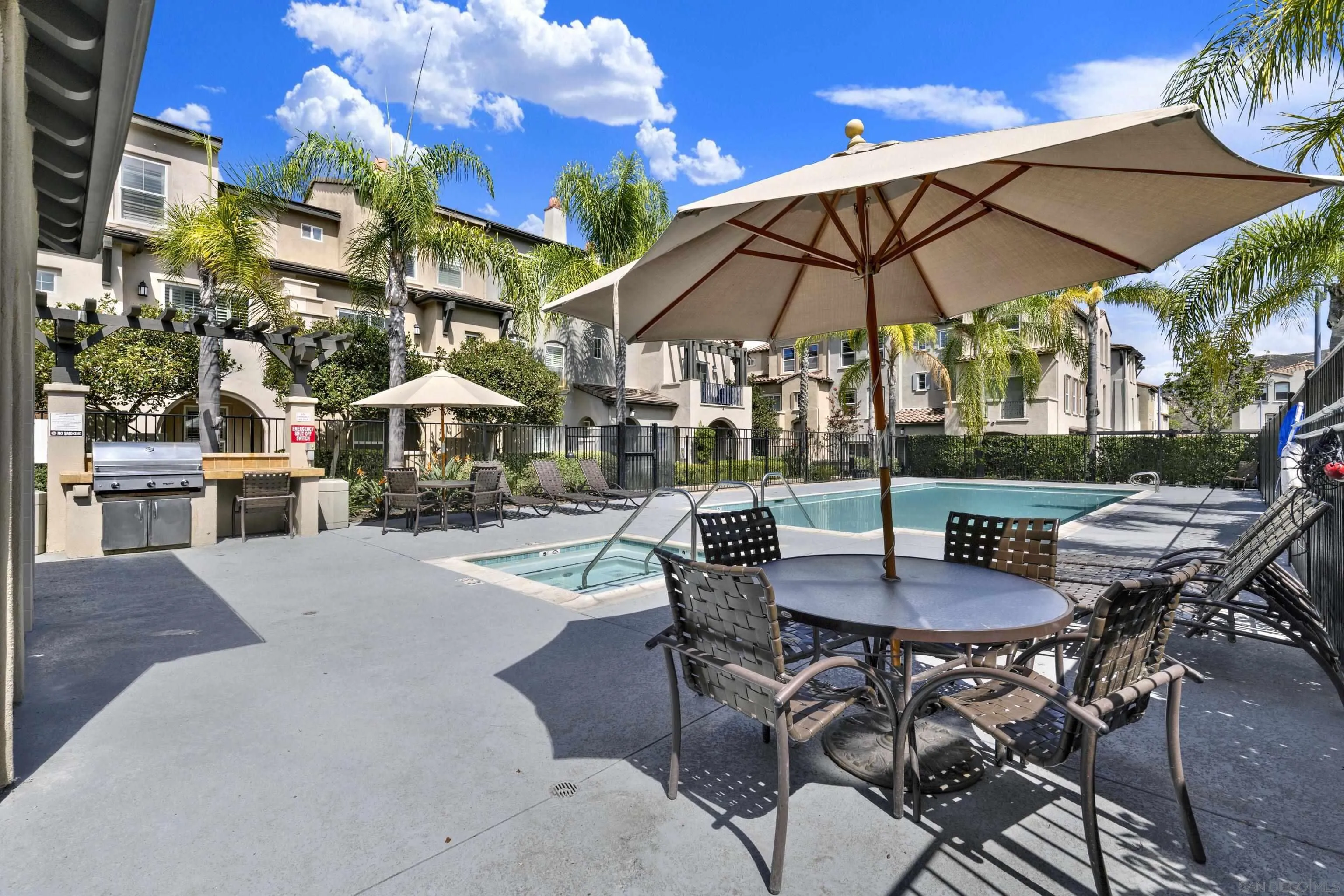 Community pool with palm trees, lounge chairs, a shaded patio table, and a built-in grill.