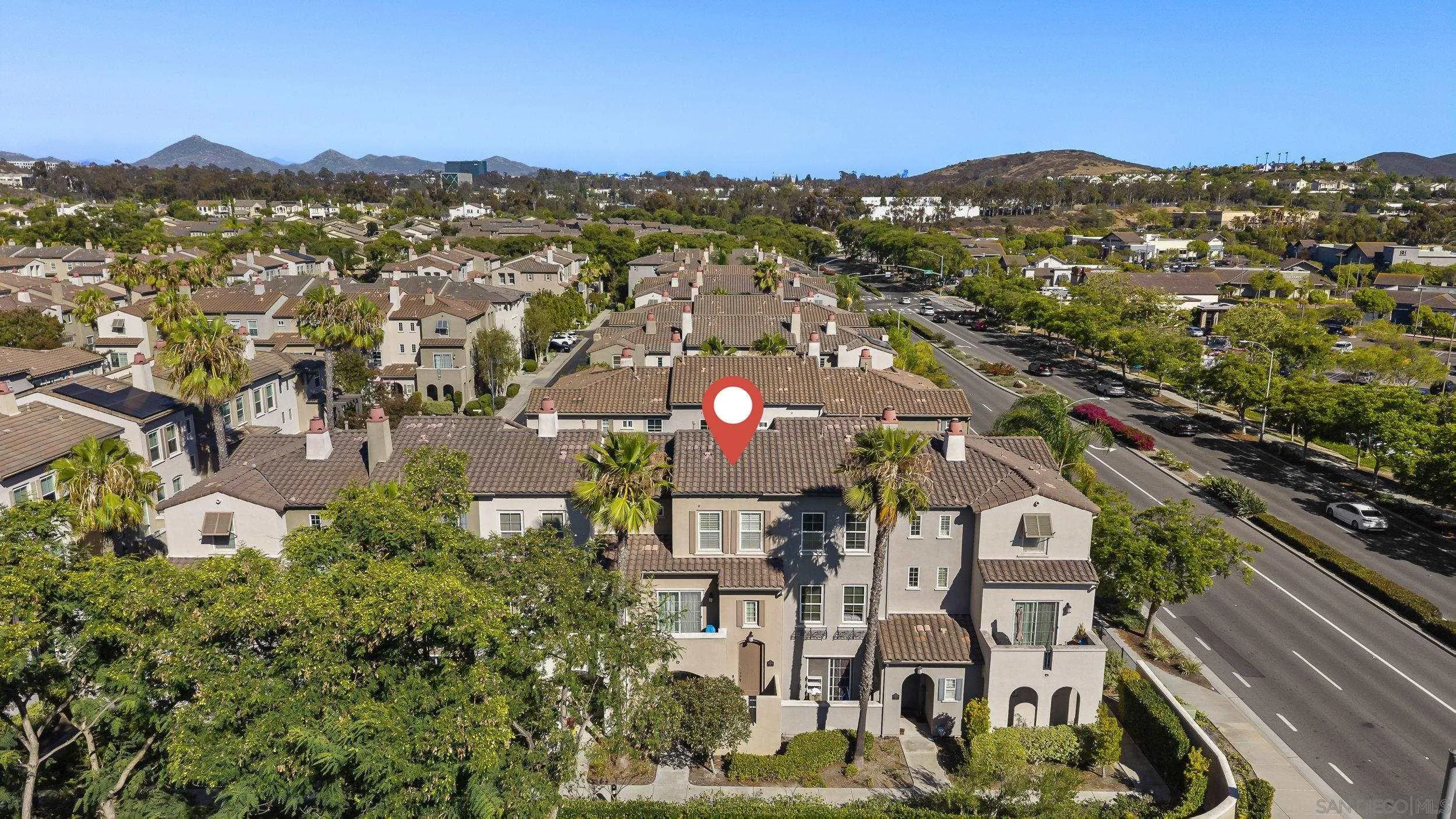 Aerial view of a San Diego townhouse marked with a red pin, among tile-roof homes and palm trees.