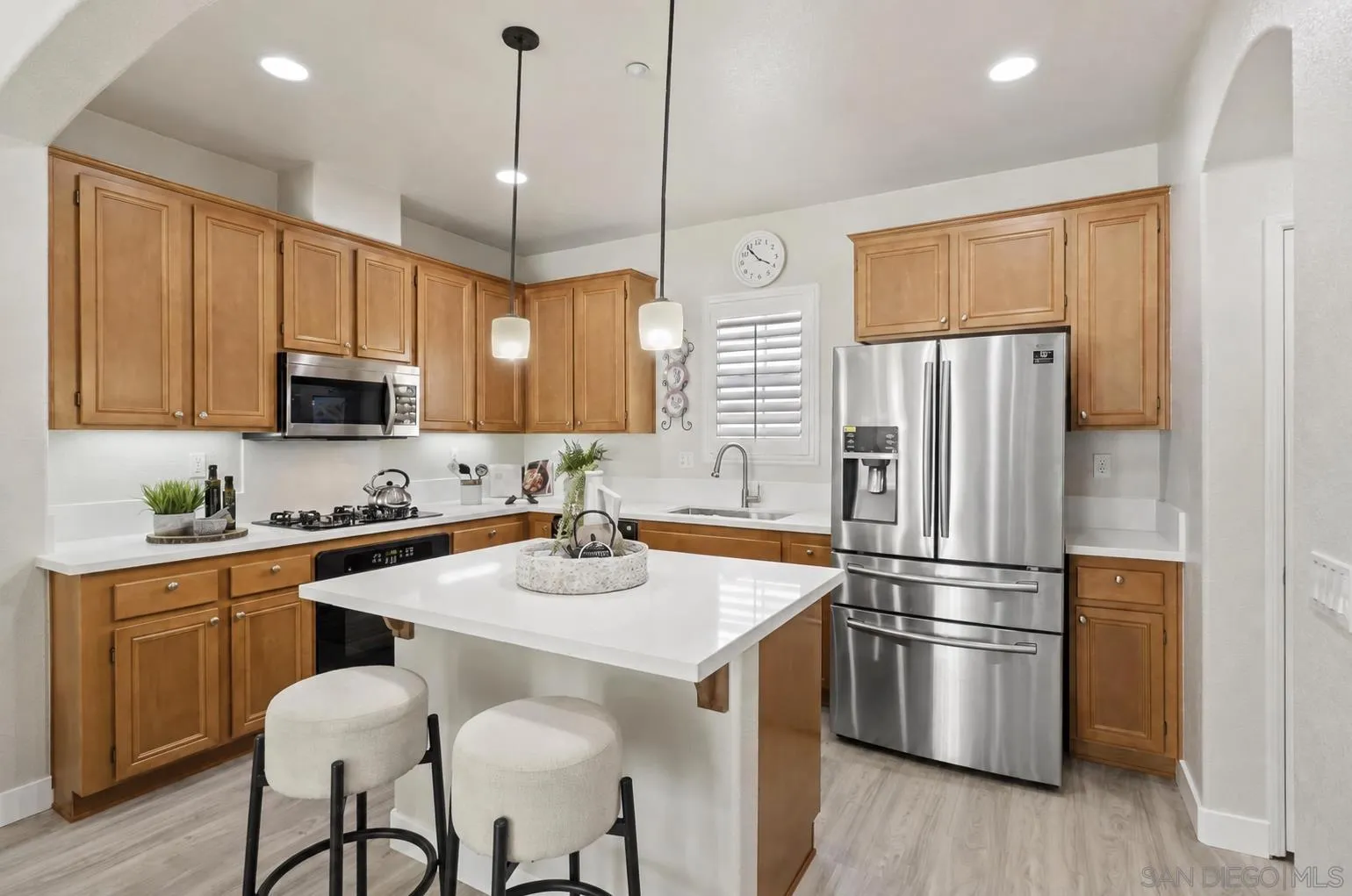Kitchen with a white island, two stools, honey-colored cabinets, and stainless steel appliances.