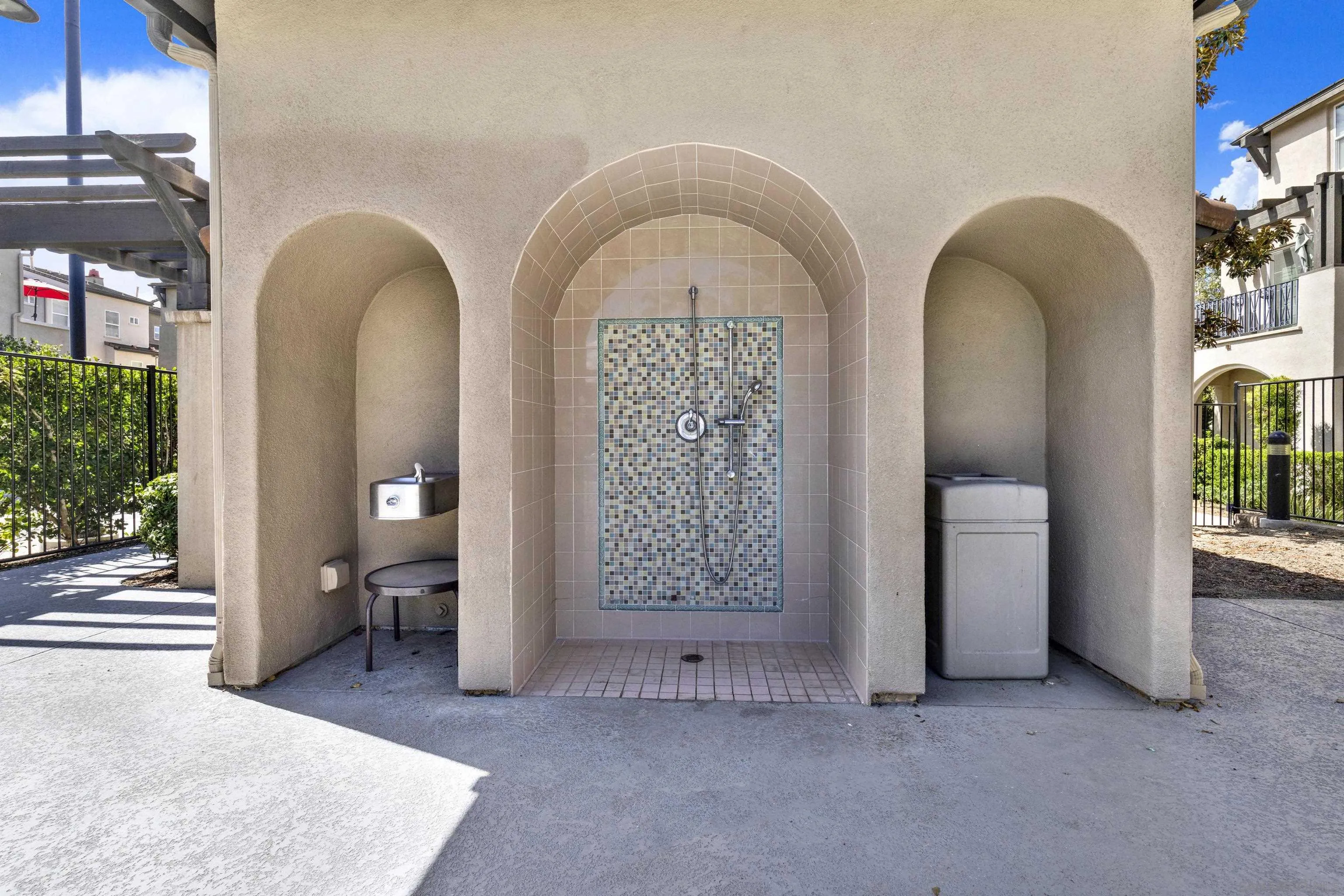 Outdoor tiled shower with a mosaic feature wall, drinking fountain, and covered trash receptacle.