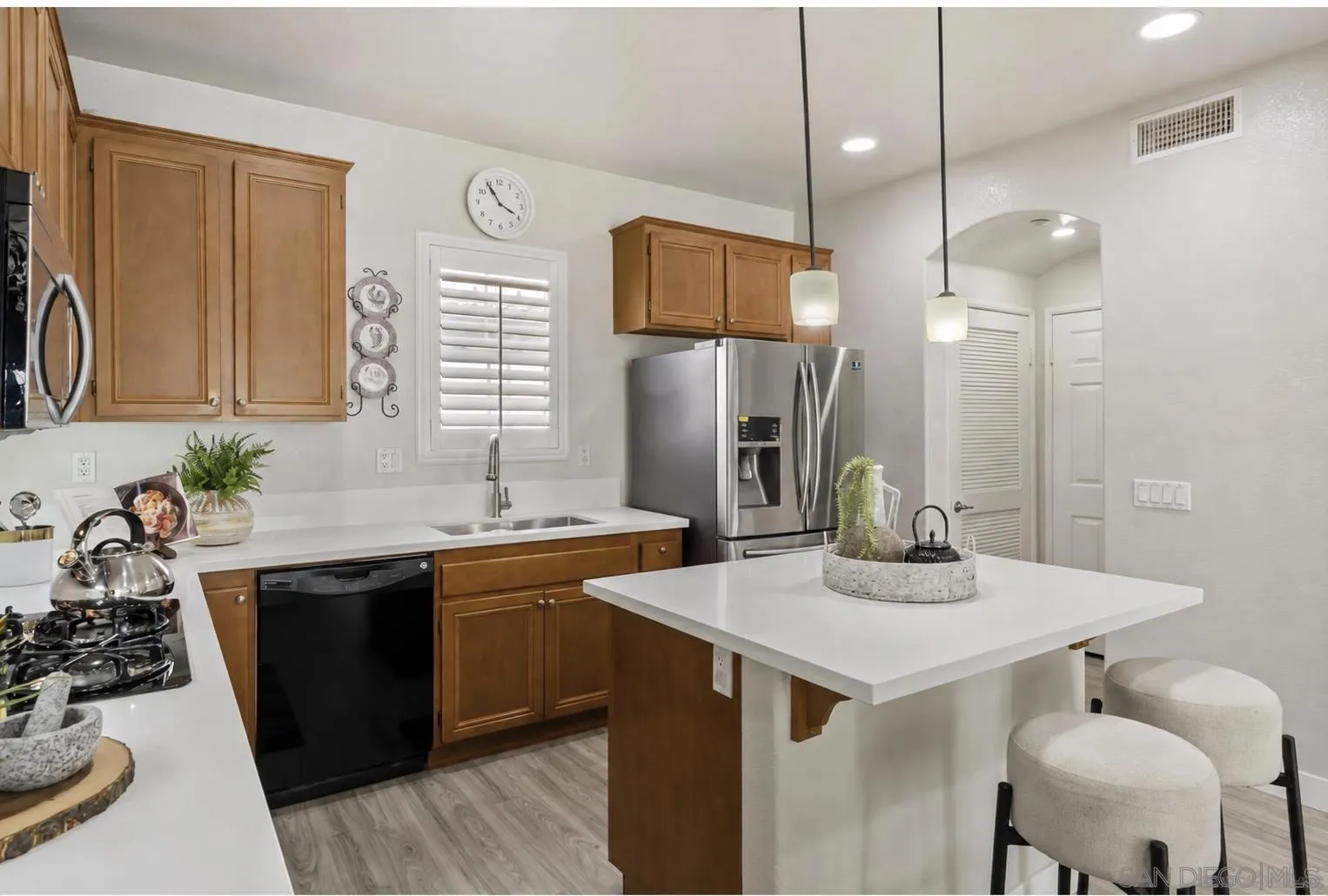 Kitchen with warm wood cabinets, stainless steel appliances, and a white island with two stools.