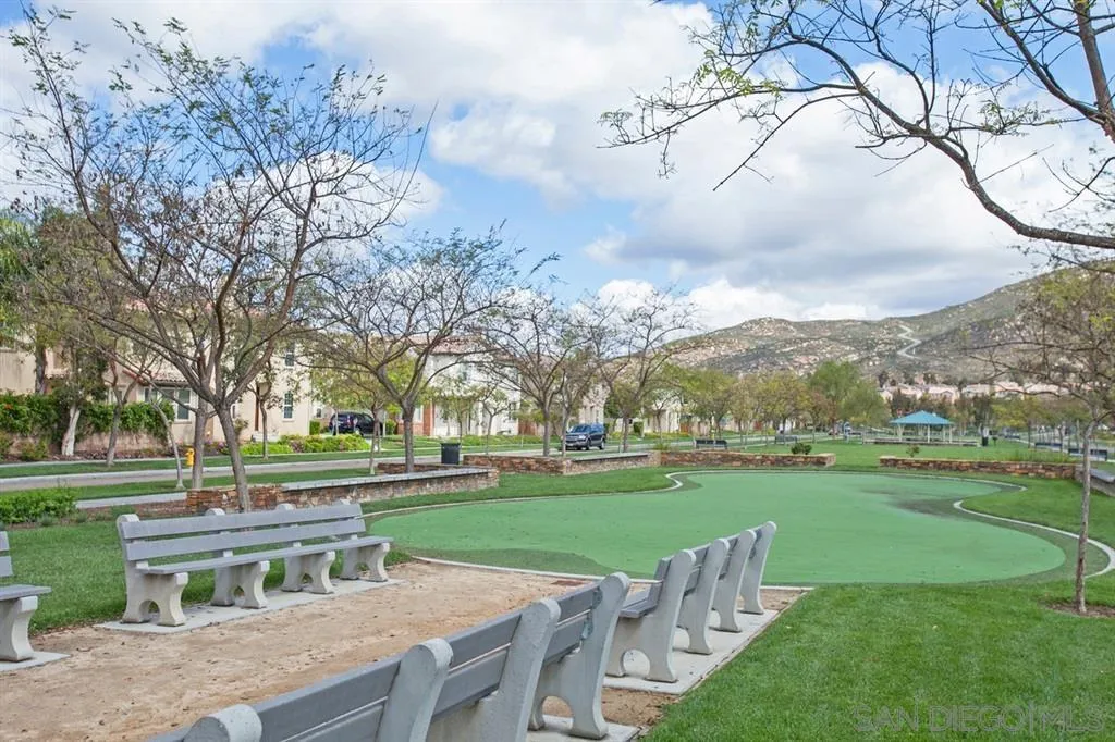 Community park with a green lawn game area, rows of benches, and distant hills.