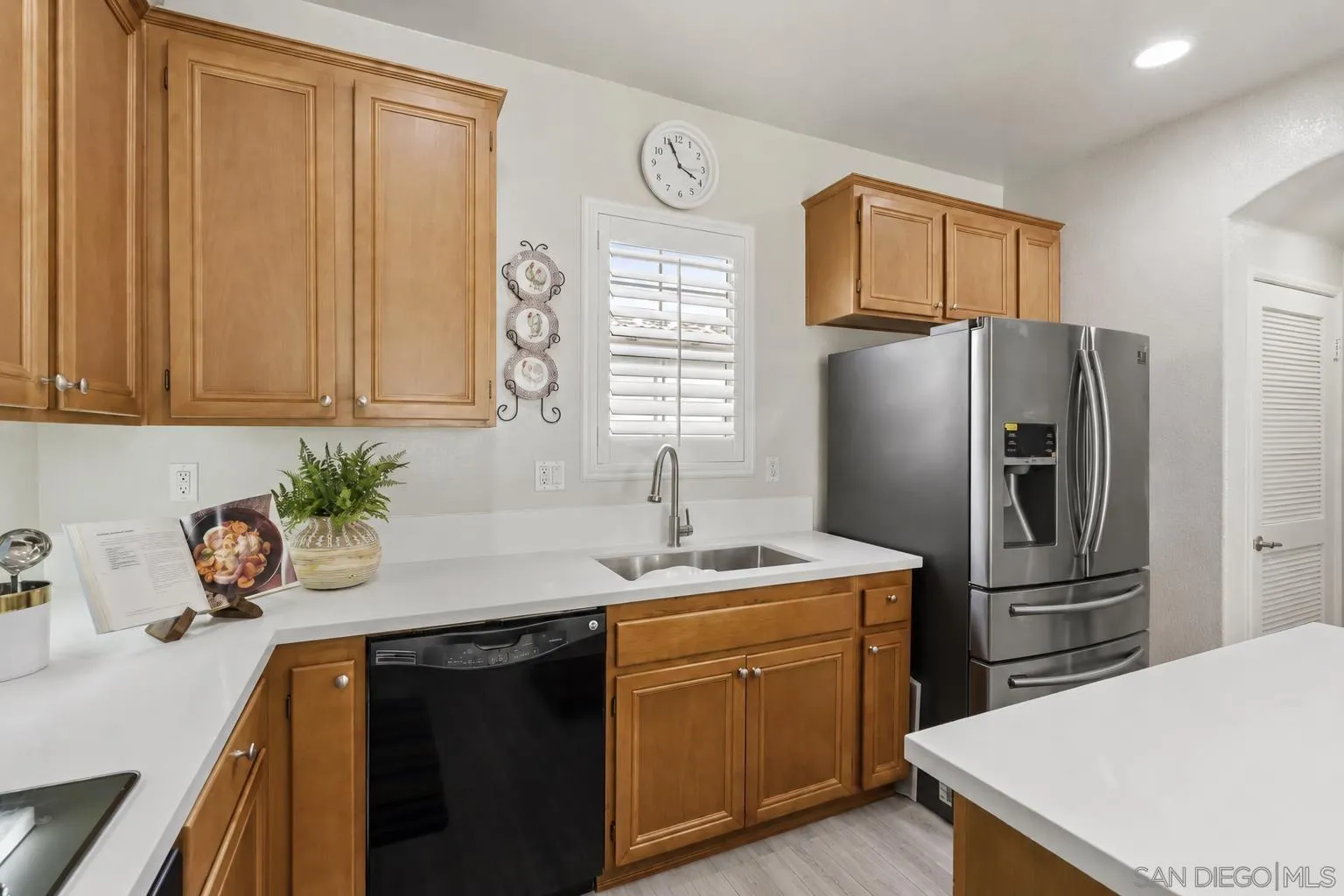 Kitchen with warm wood cabinets, white countertops, stainless-steel refrigerator, and a sink beneath shuttered window.