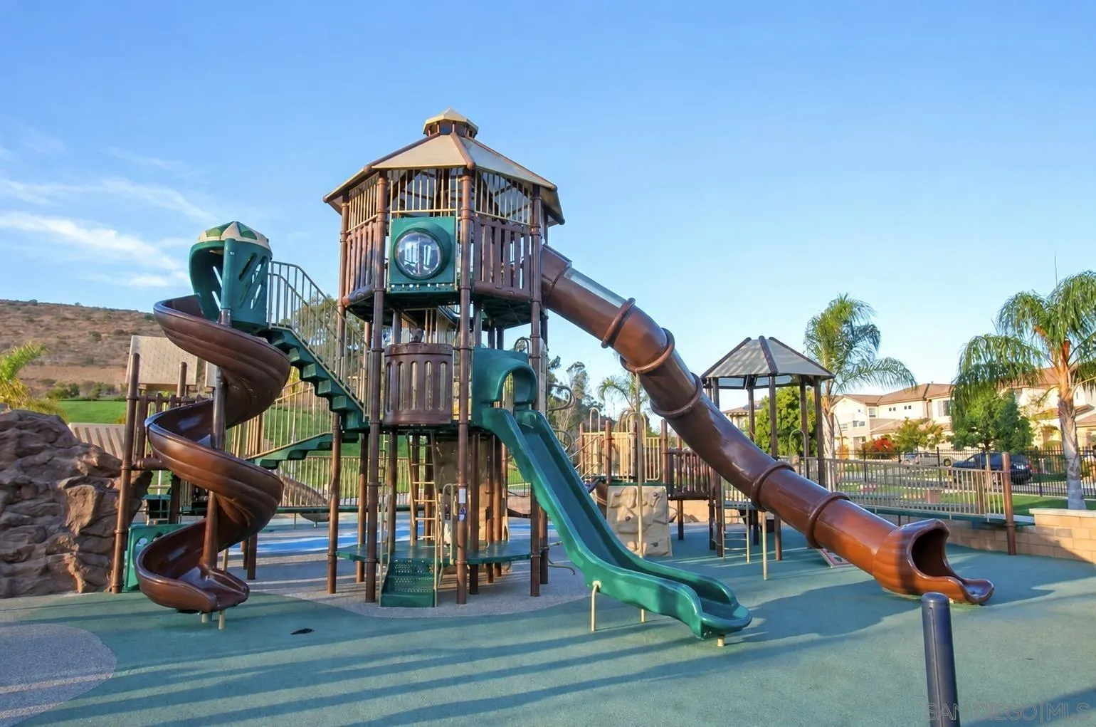 Community playground with a multilevel play structure, twisting tube slides, and a shaded gazebo.