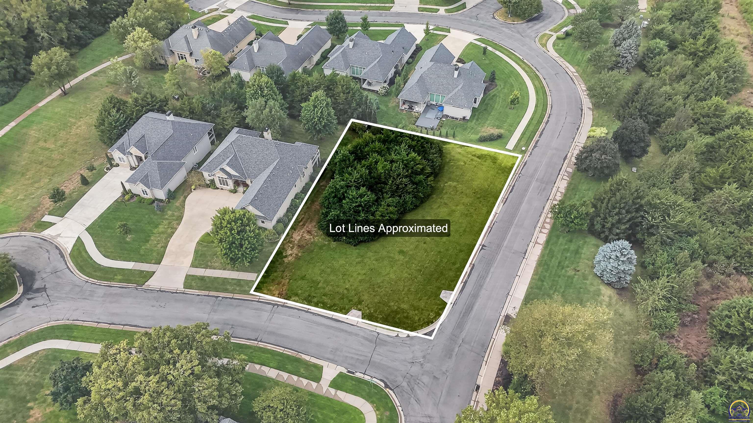 Aerial view of a vacant, tree-lined lot outlined at a residential street corner.