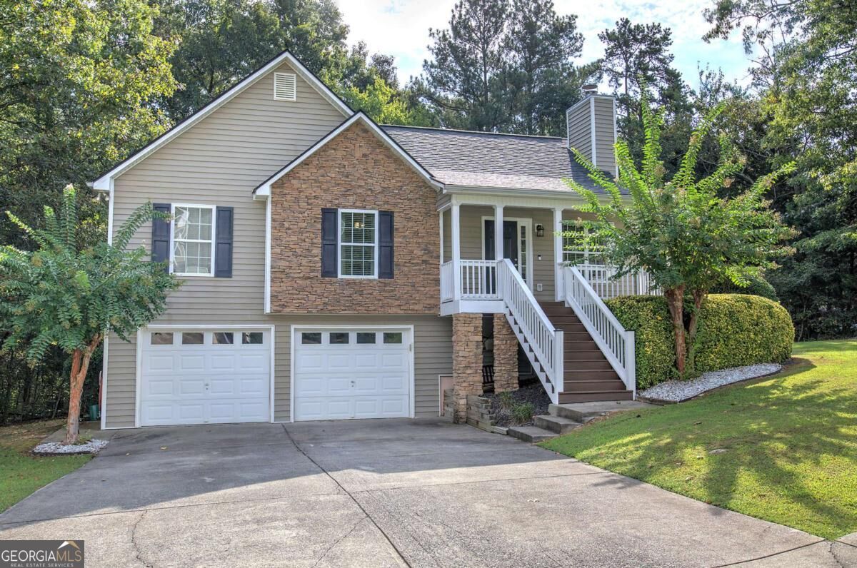 Split-level home with stone facade, two garage doors, and a raised porch with white railings.