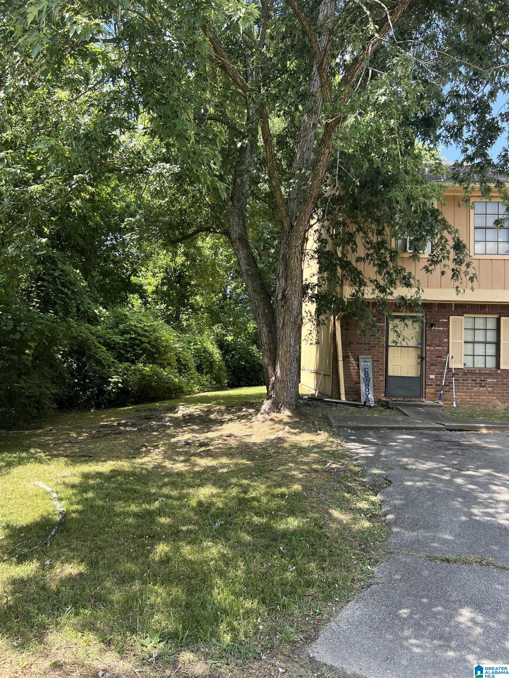 Home exterior partly shaded by a large tree, with a lawn and driveway.