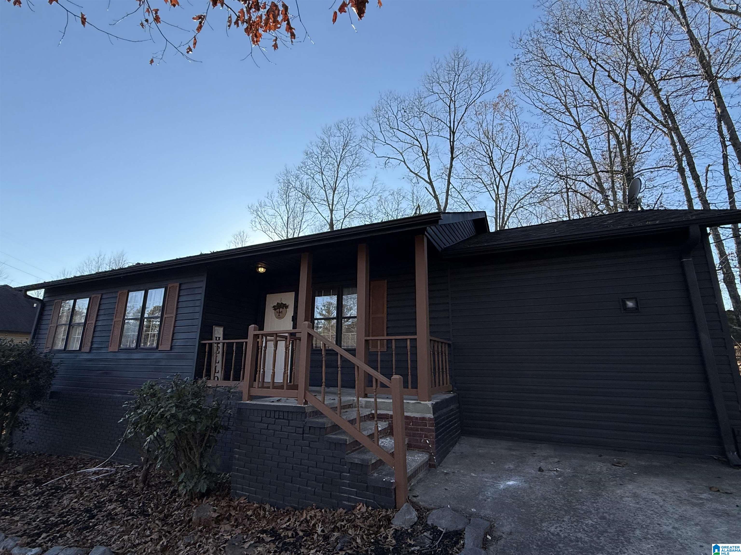 Dark-sided single-story home with a covered porch, brown shutters, and a wide concrete driveway.
