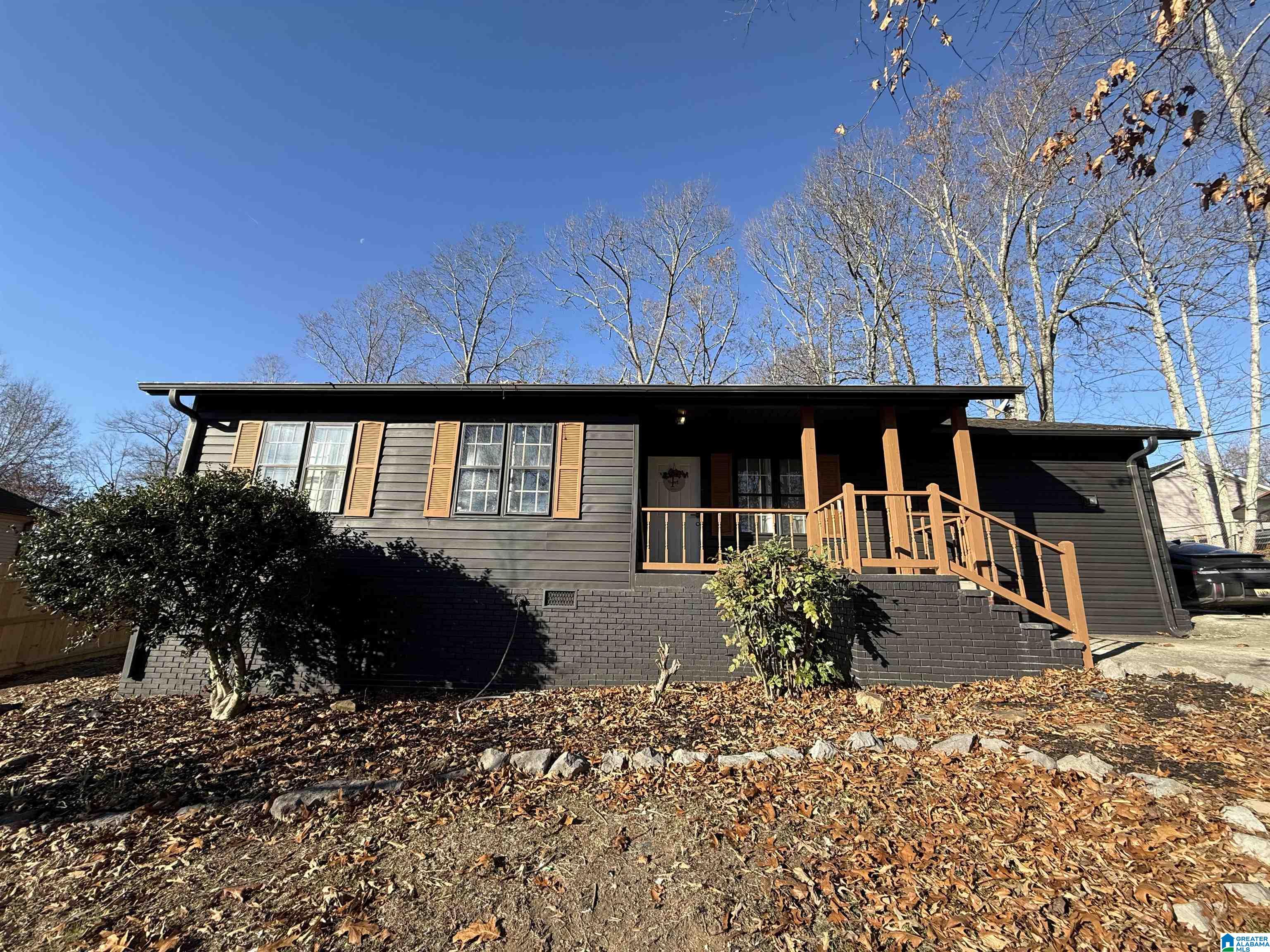 Dark single-story home with orange shutters and a covered porch above a leaf-covered yard.