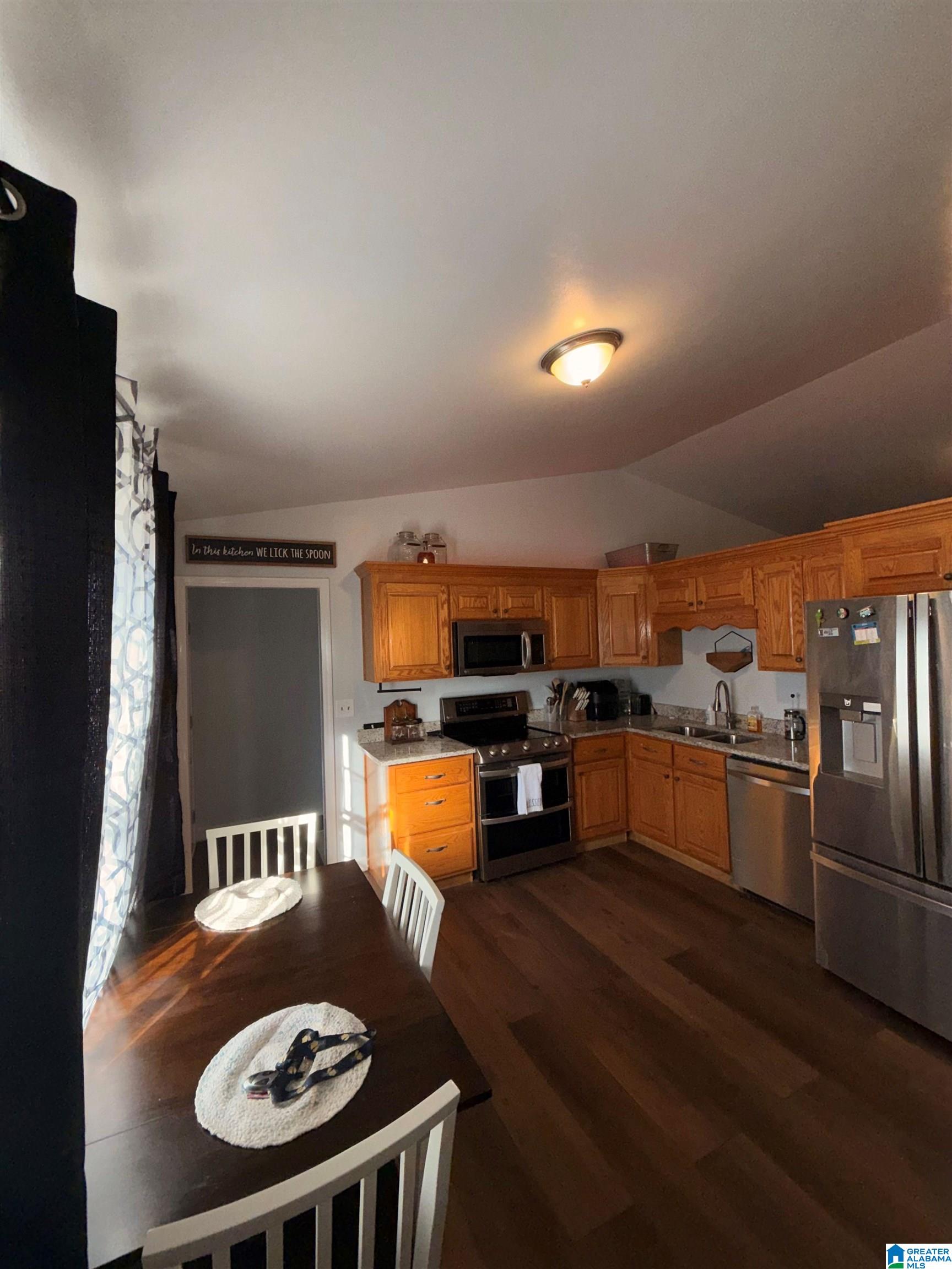 Kitchen with honey-colored cabinets, granite counters, stainless steel appliances, and an adjoining dining table.