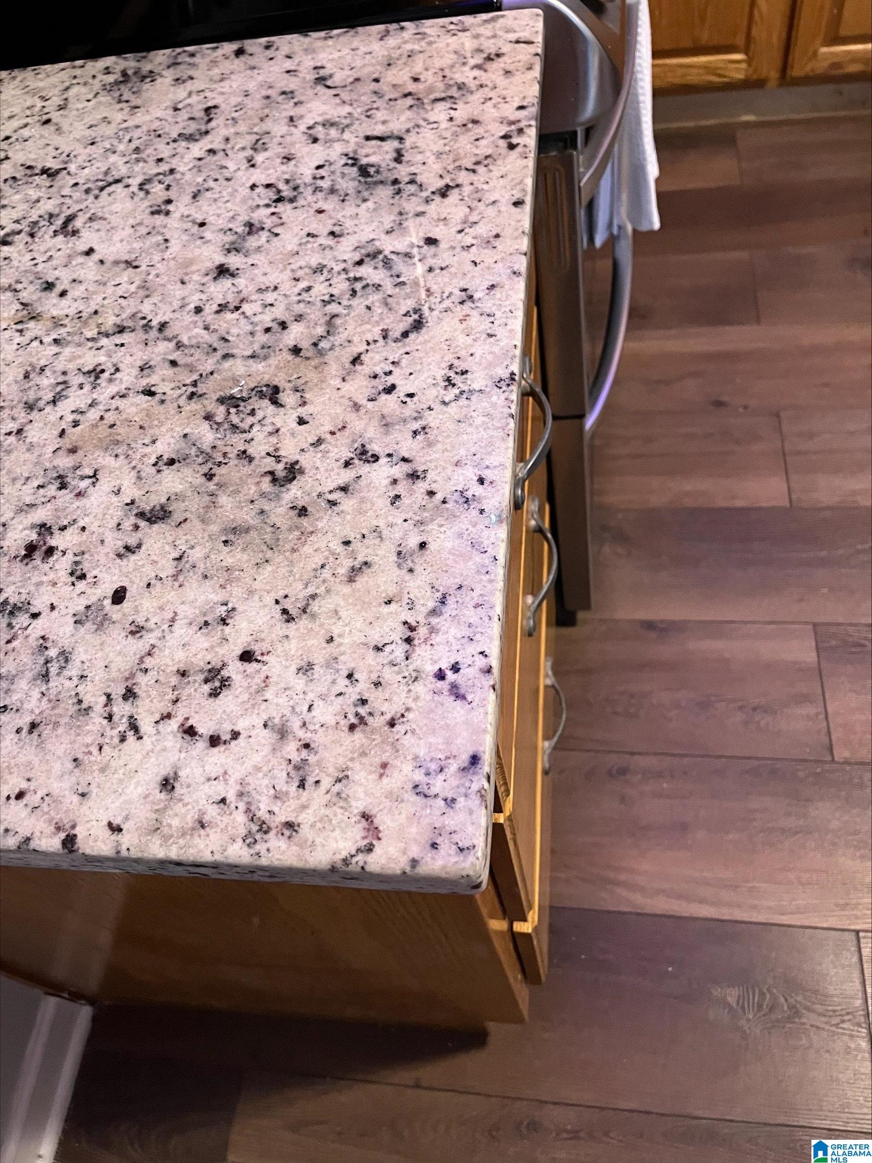 Speckled stone kitchen countertop above wood cabinets and dark plank flooring.