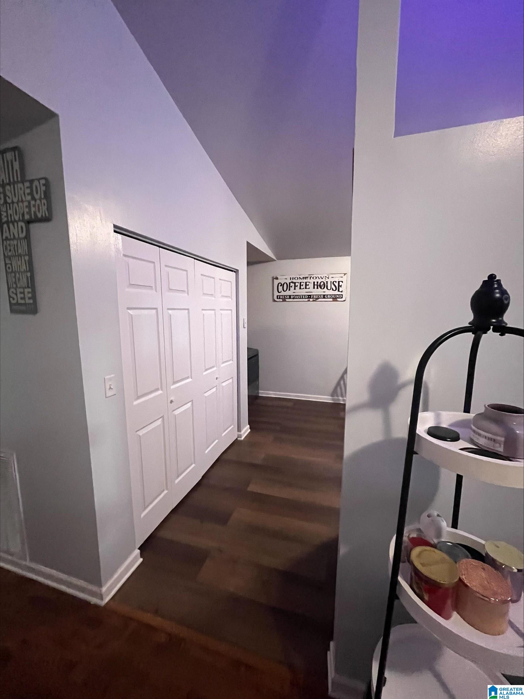 Hallway with white double closet doors, dark wood floors, and a coffee-house sign.