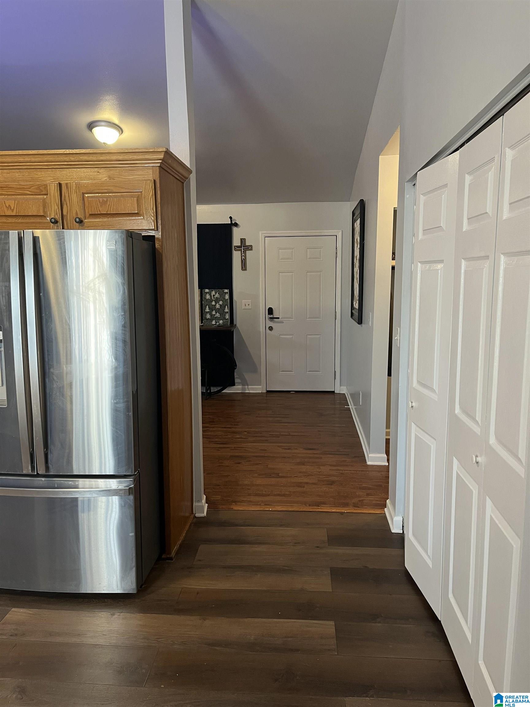 Kitchen and hallway with stainless steel refrigerator, oak cabinets, and dark wood floors.