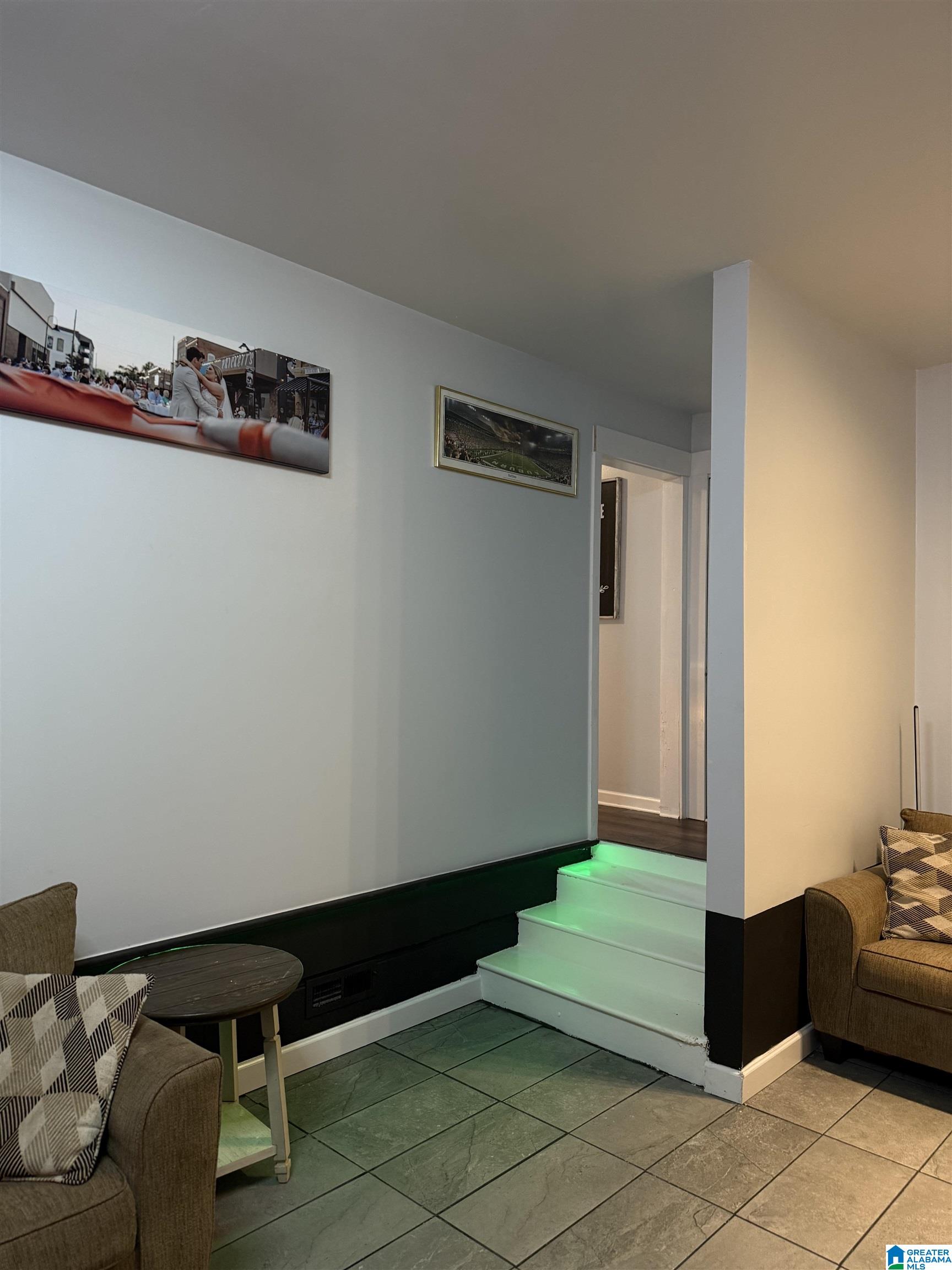 Furnished living room with green-lit steps, gray tile flooring, and brown sofas.