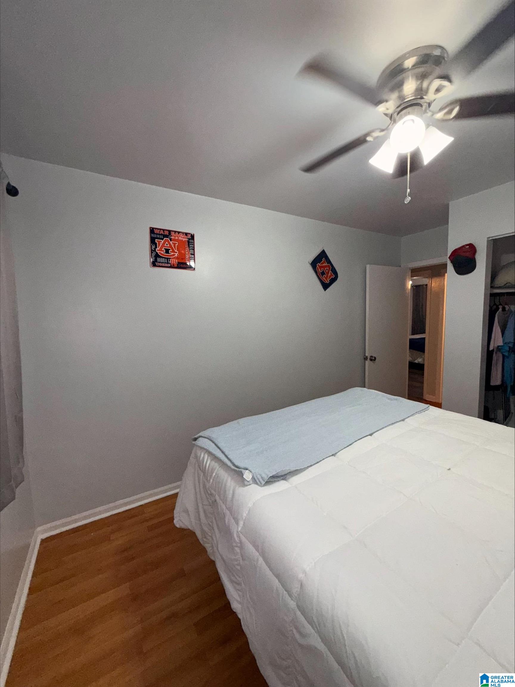 Bedroom with a white bed, pale blue blanket, hardwood floor, and Auburn wall decorations.