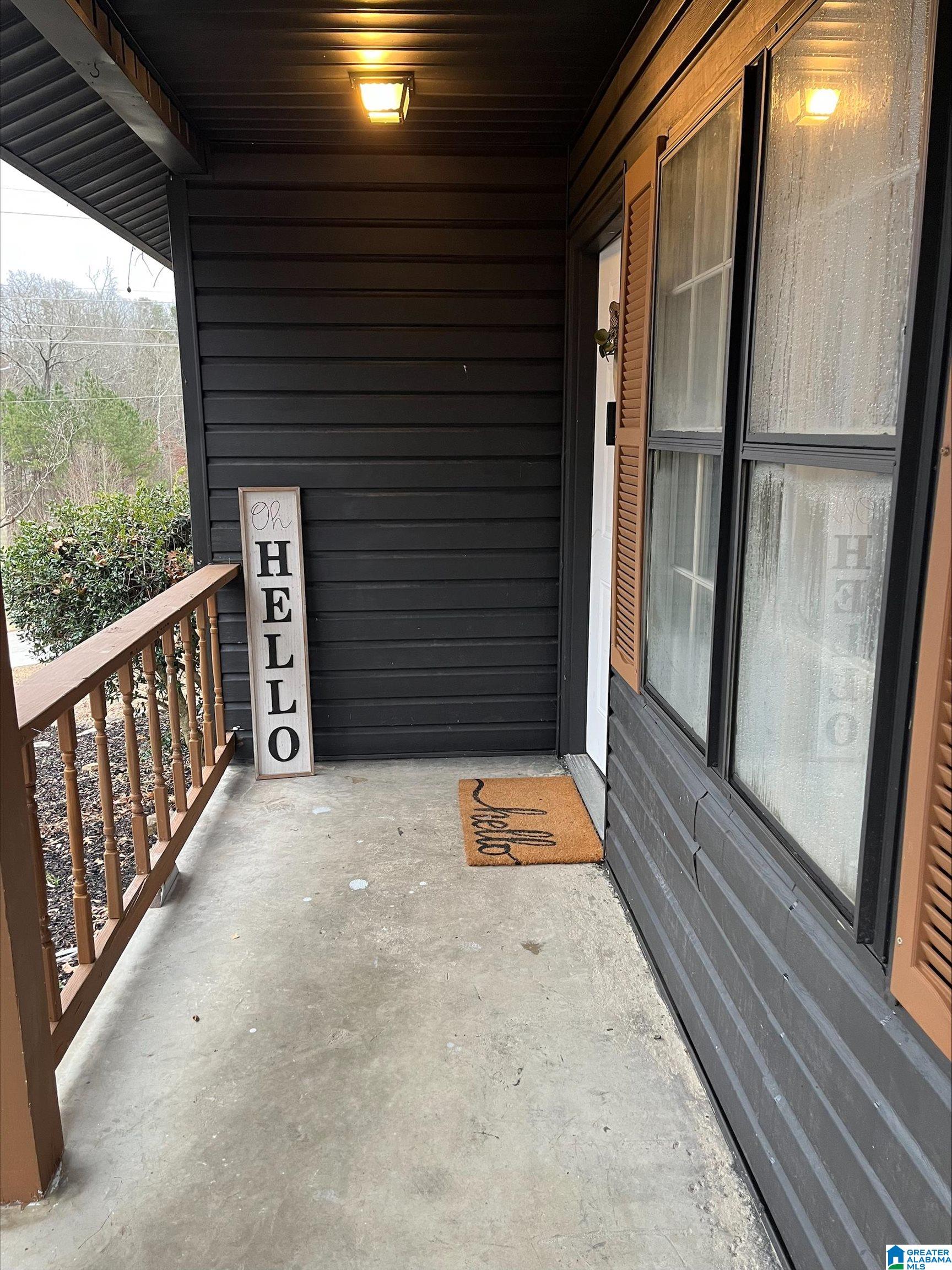 Covered front porch with dark siding, a wooden railing, and a vertical “Oh HELLO” sign by the door.