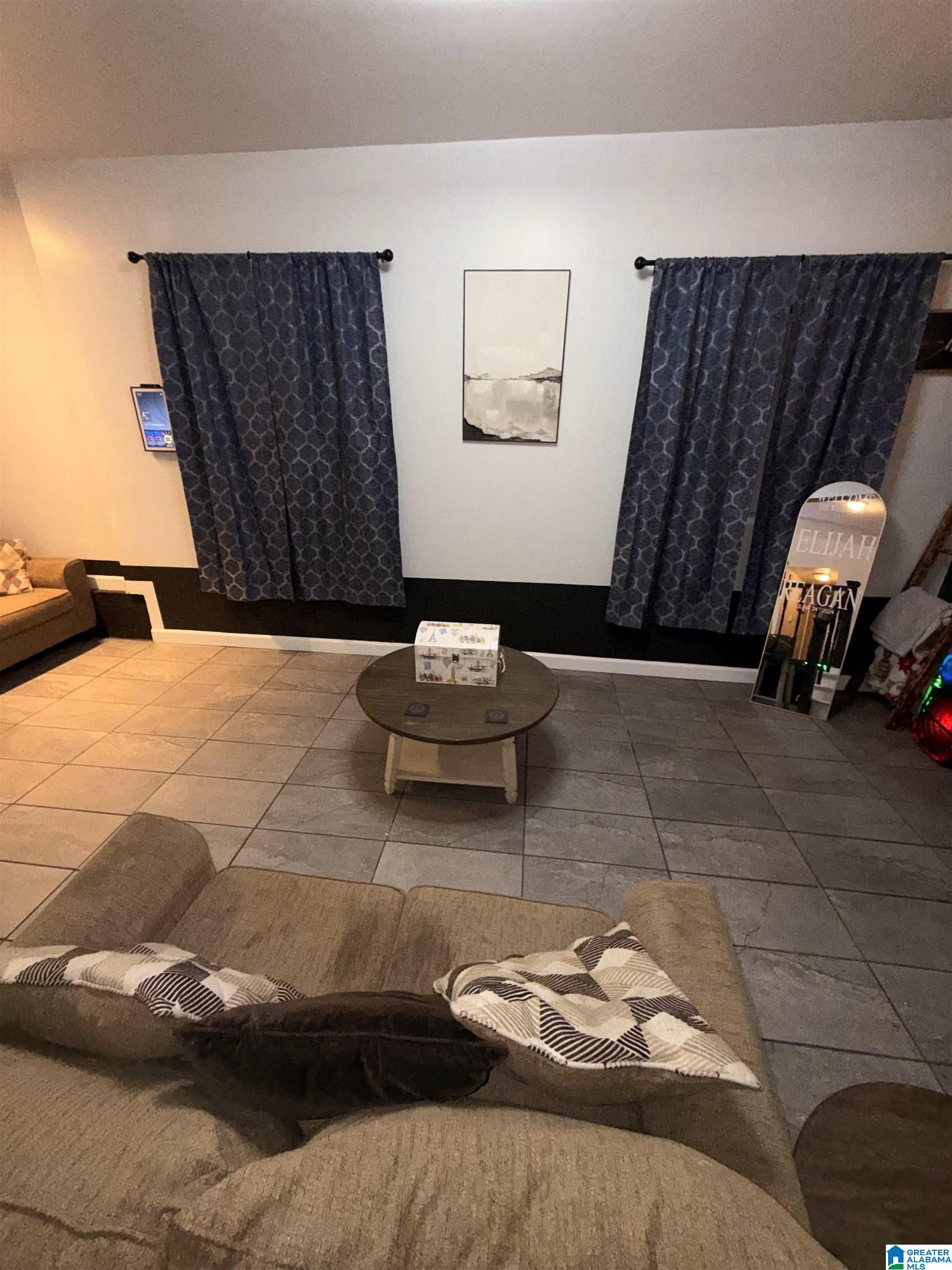 Furnished living room with a large sectional, tiled floor, round coffee table, and patterned curtains.