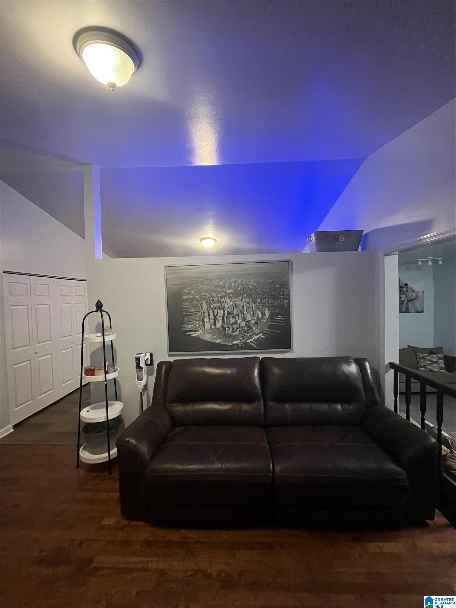 Furnished living room with a dark leather sectional, hardwood floors, and blue ceiling accent lighting.