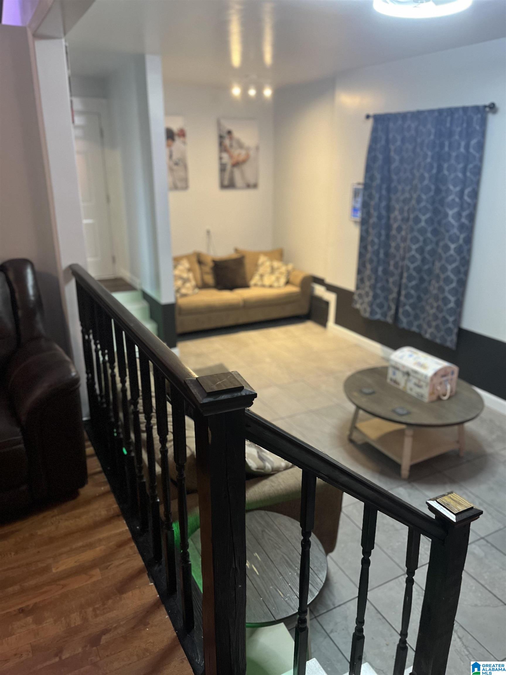 Furnished living room with a tan sofa, blue curtains, and a black railing between two flooring levels.