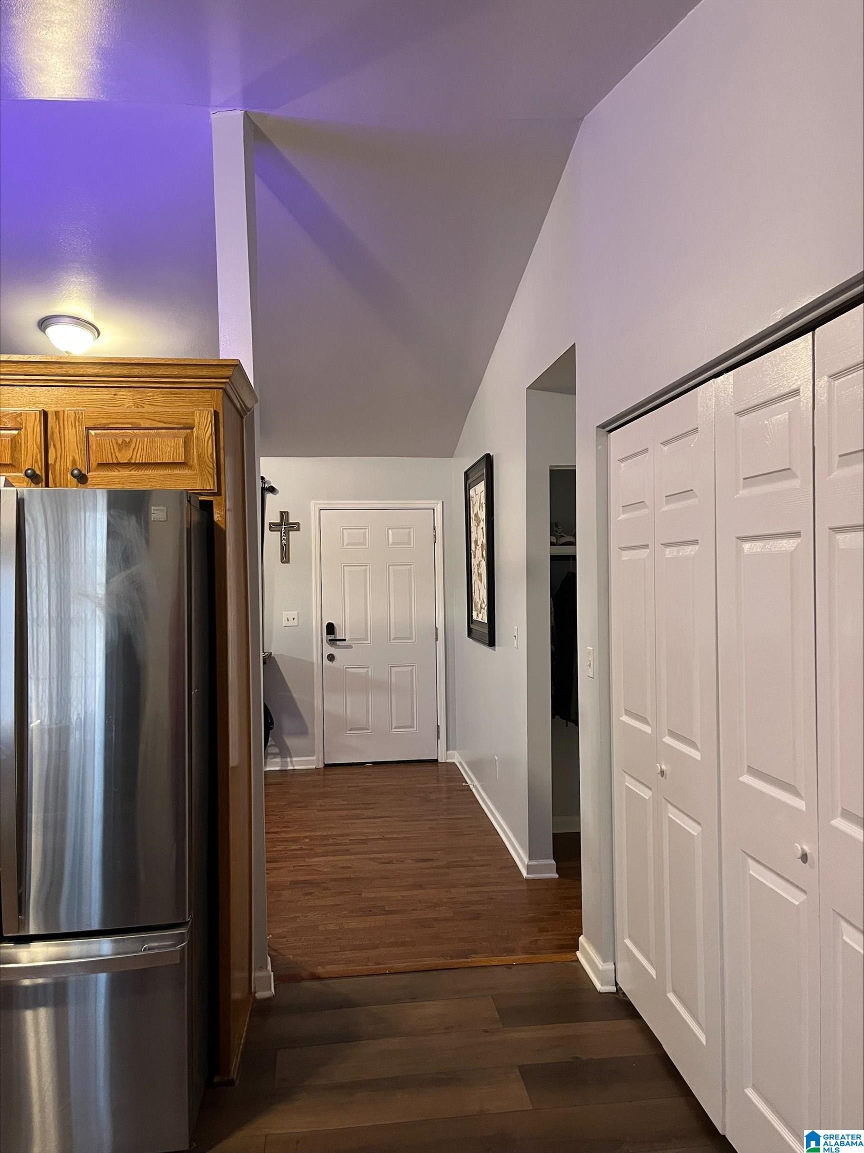 Entry hallway with dark wood floors, white closet doors, and a stainless steel refrigerator.