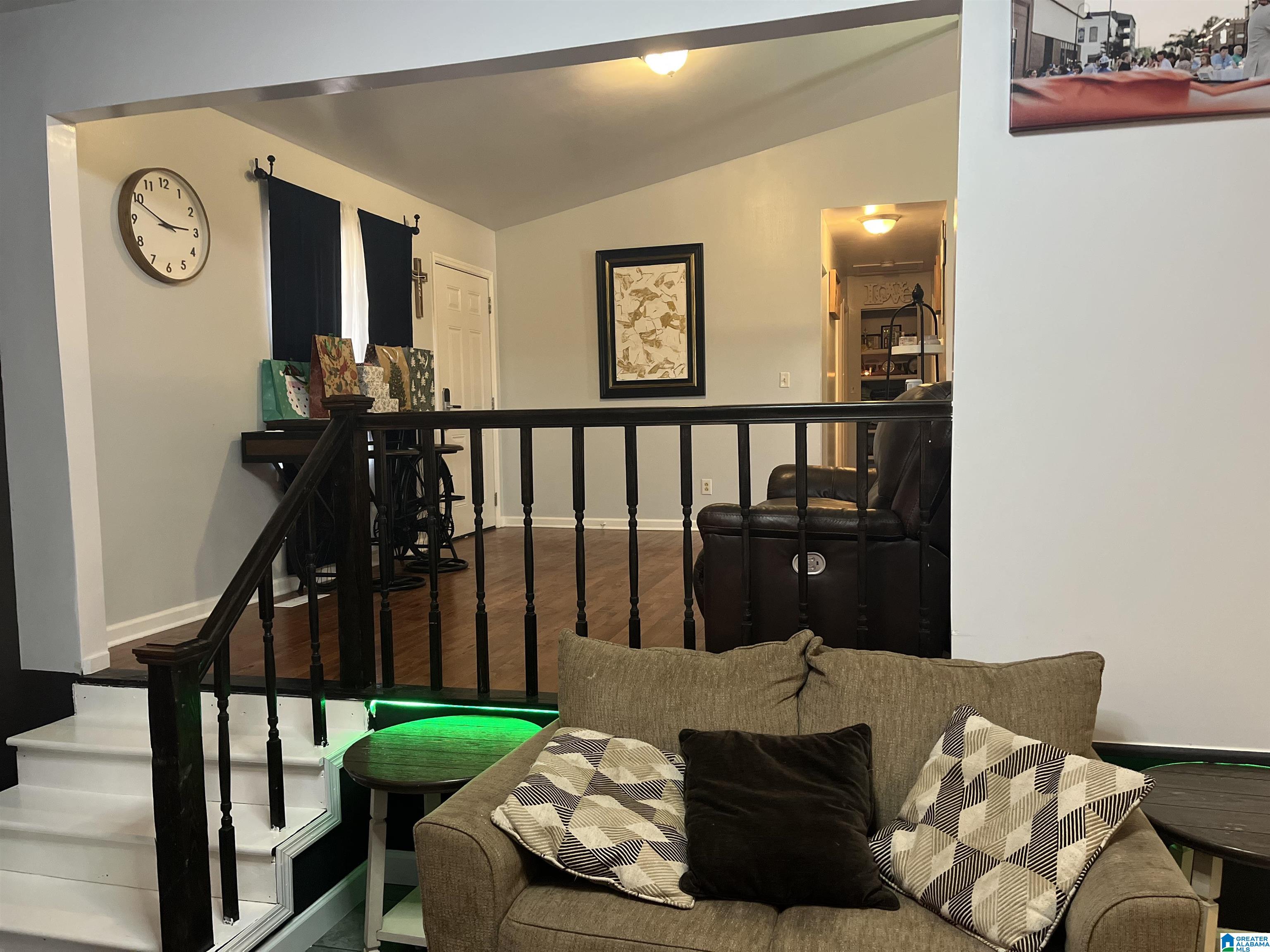 Furnished living room with a brown sofa, black stair railing, and green accent lighting.