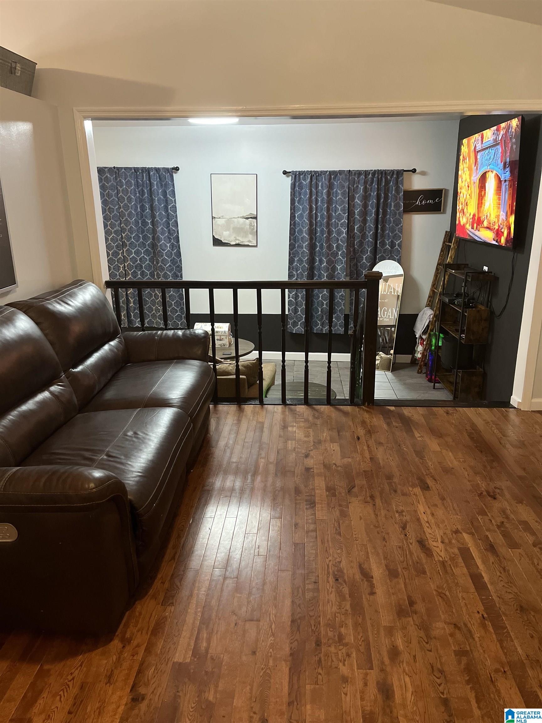 Furnished living room with a leather sectional, hardwood floors, and a railing overlooking a tiled area.