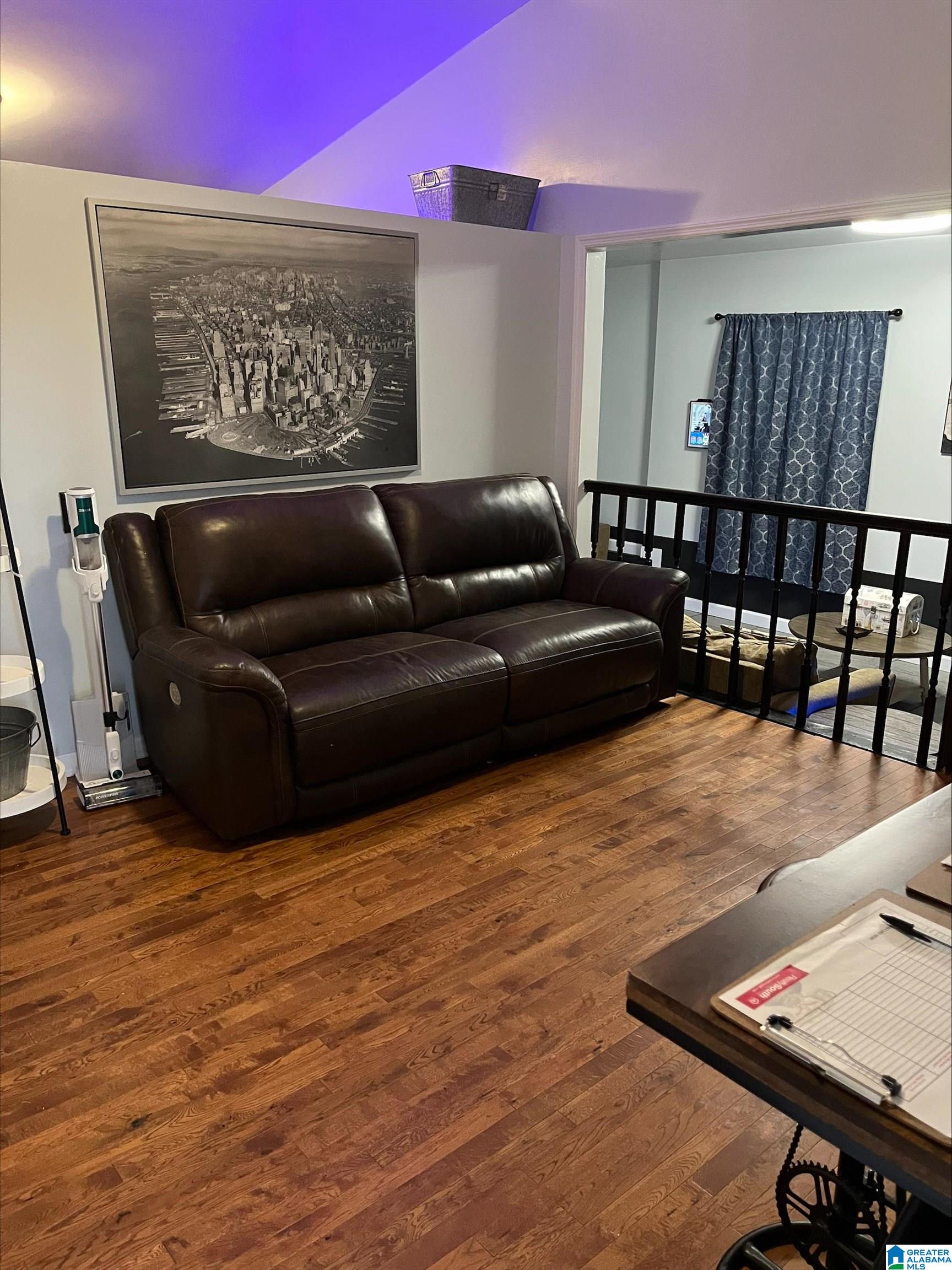 Living room with a dark leather sofa, hardwood floors, and purple accent lighting.