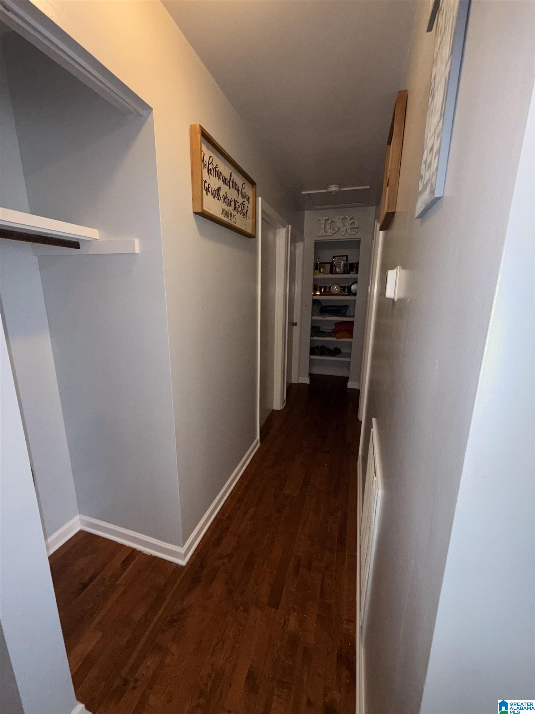 Hallway with dark hardwood floors, gray walls, wall art, and built-in display shelves.