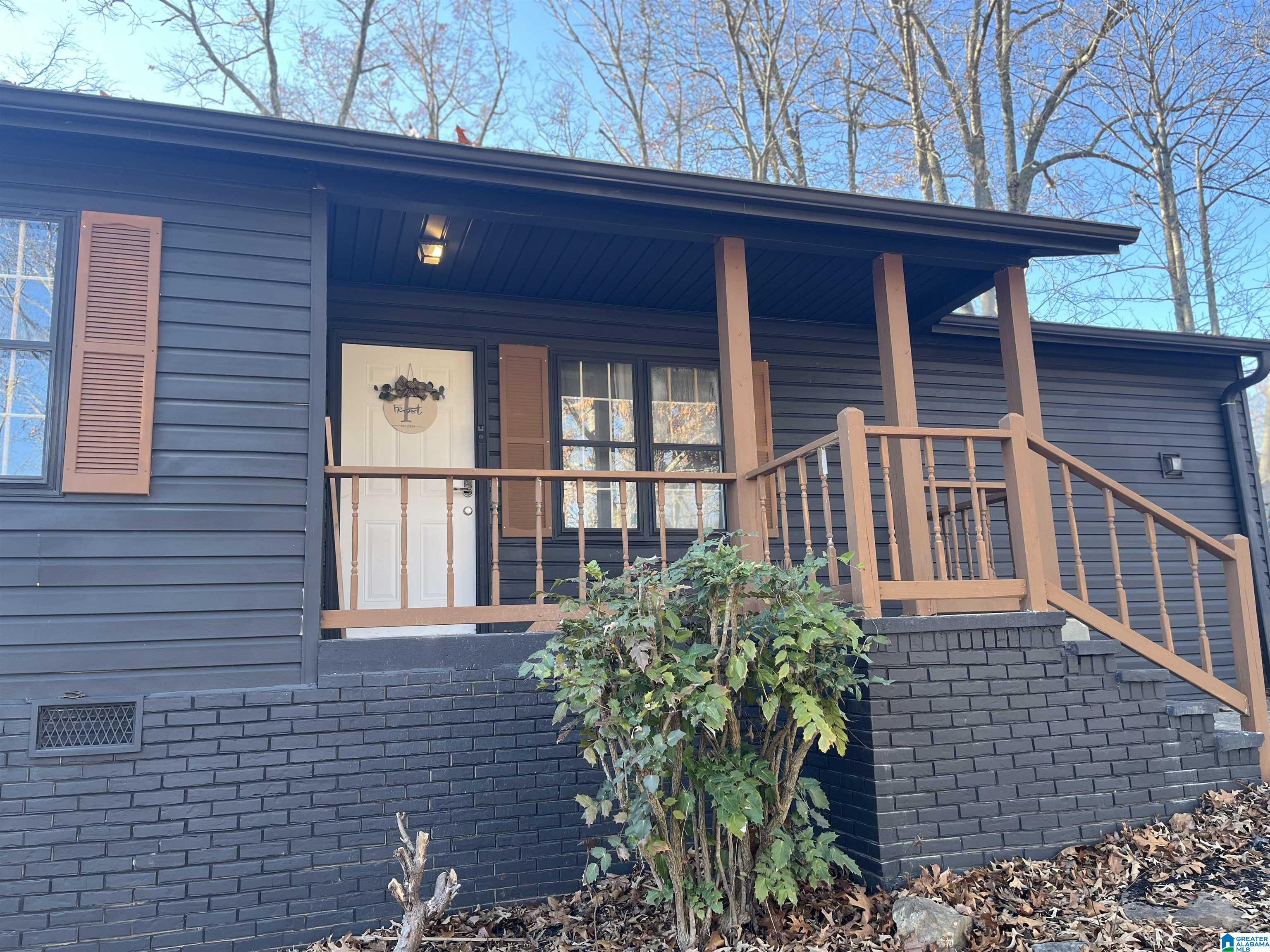 Dark blue home with a covered porch, brown railings, and a leafy shrub in front.