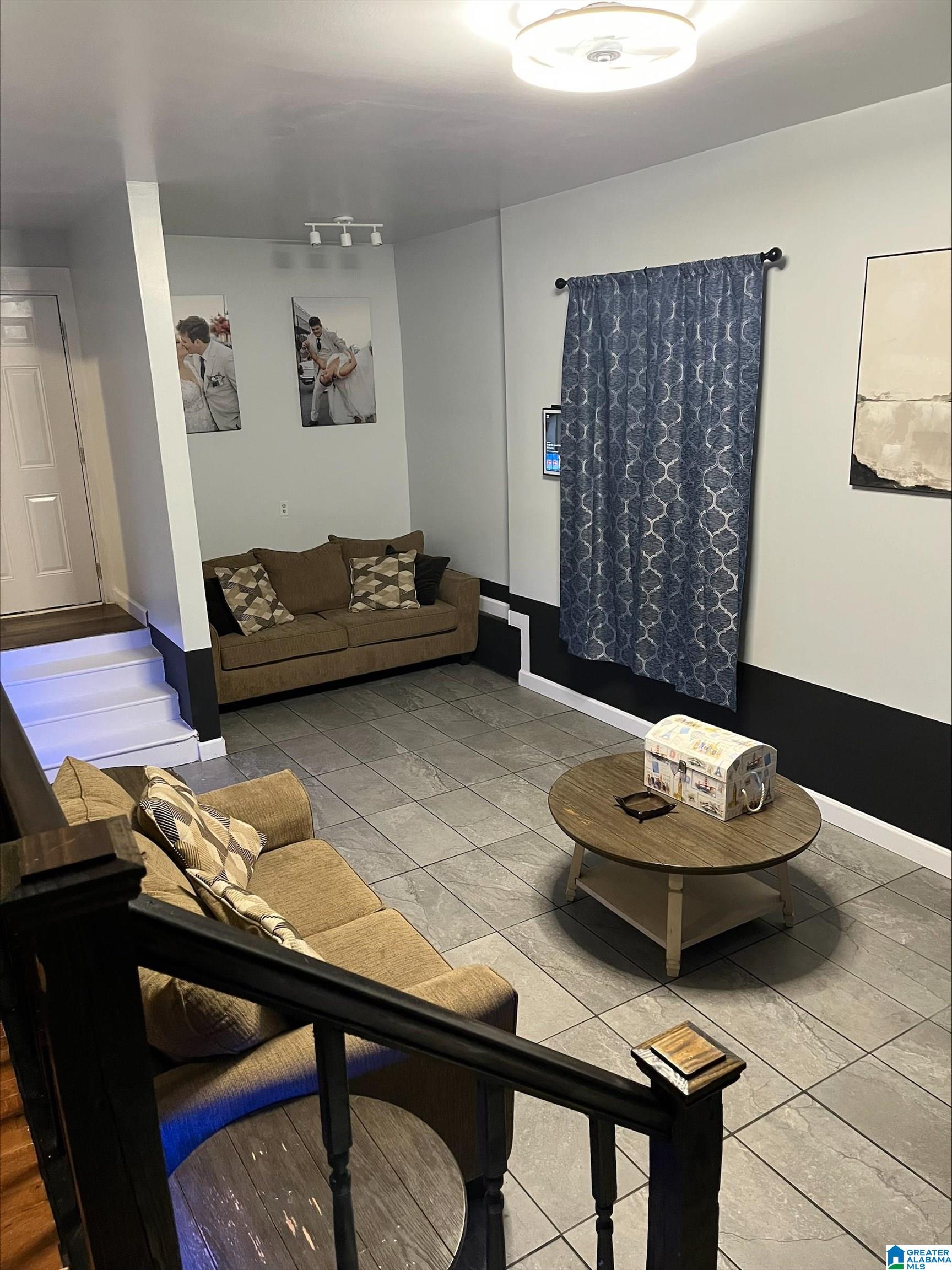 Living room with brown sofas, gray tile flooring, blue curtains, and a round coffee table.