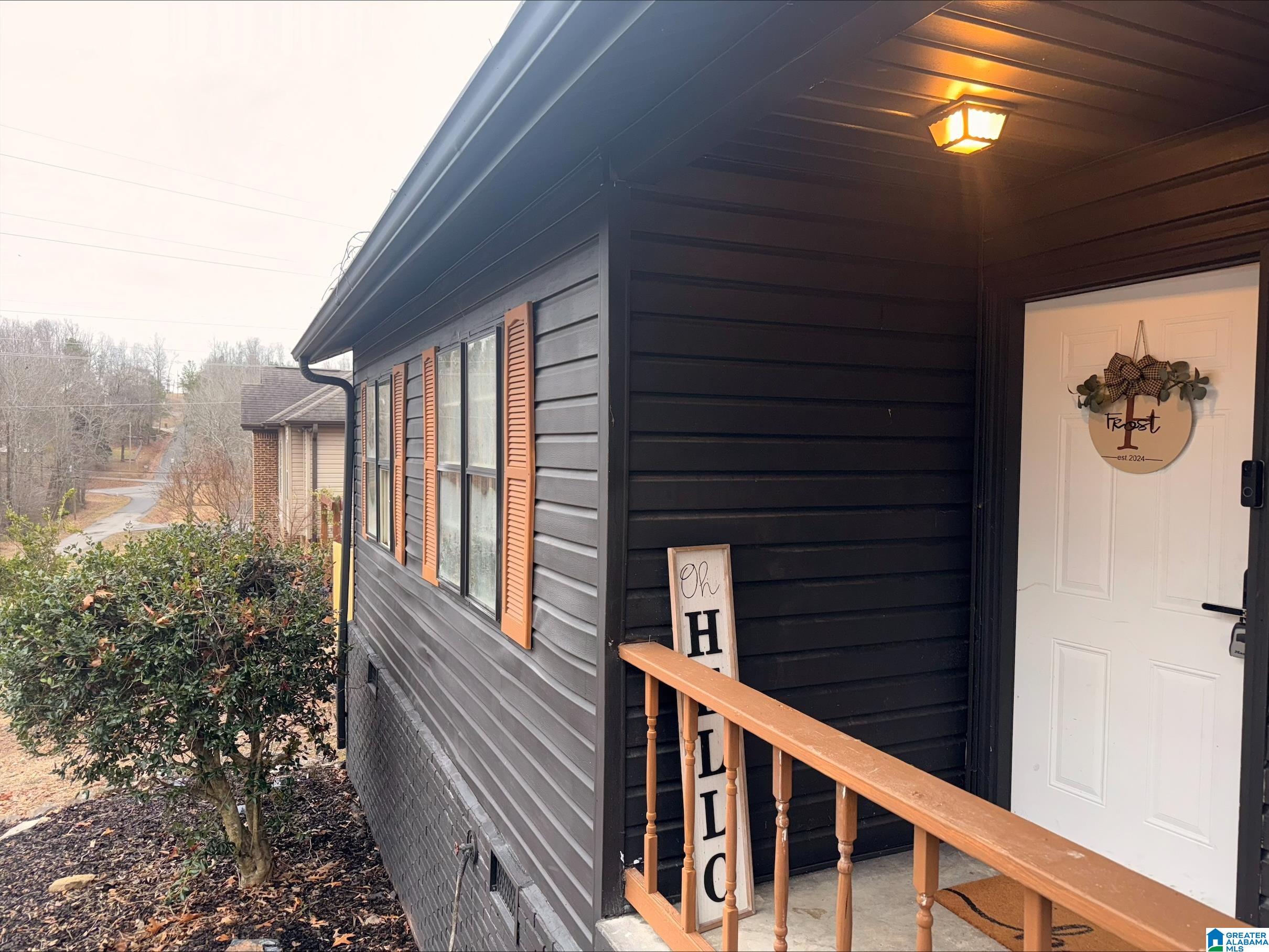 Dark-sided home entry with white door, wreath, wooden railing, and orange shutters.