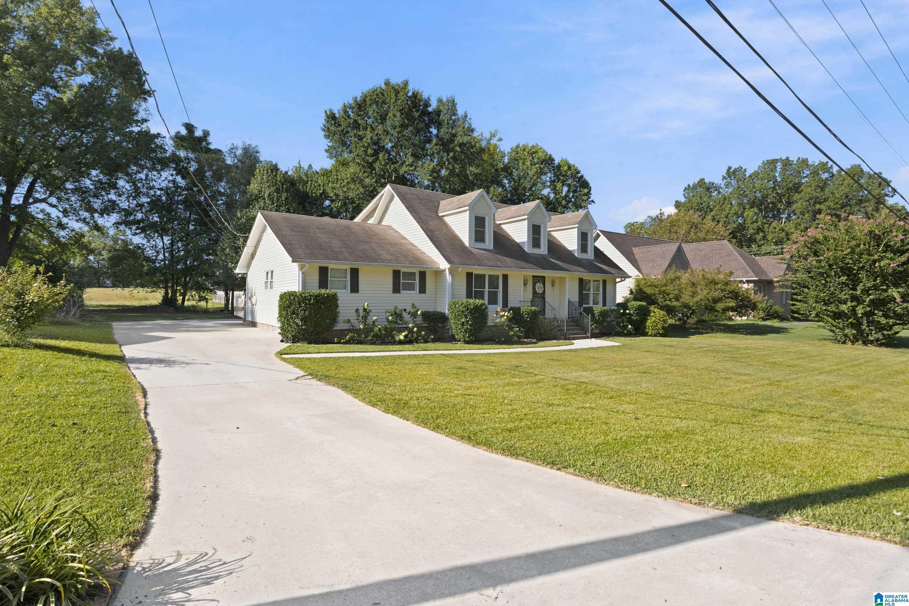 White house with three front dormers, a broad driveway, and a large green lawn.