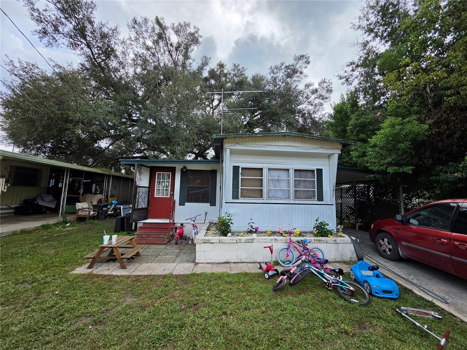 White manufactured home with a red door, green shutters, and a flower bed in front.